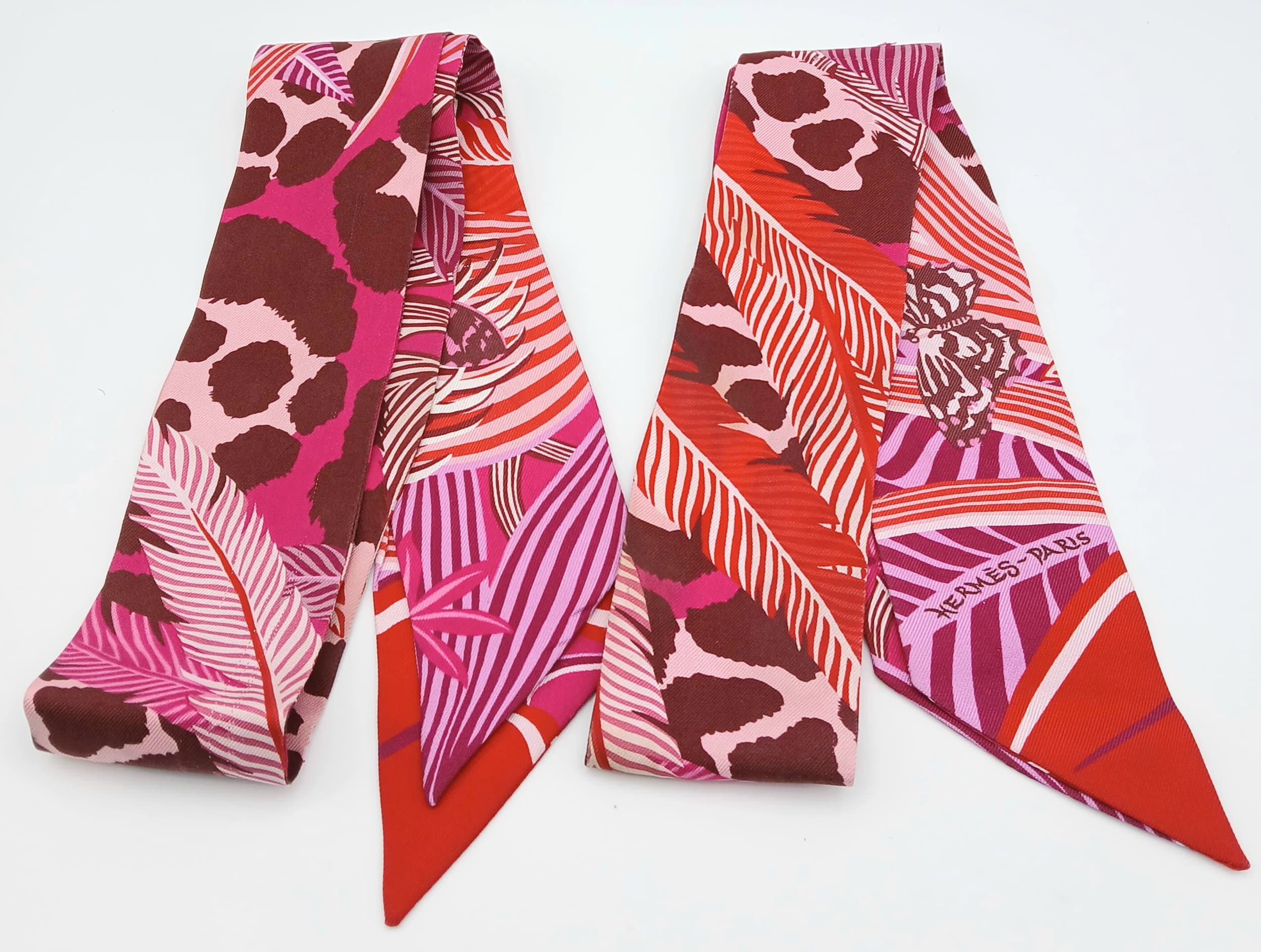 Two Hermès “Jaguar Quetzal” Twilly Scarves. In a vibrant pink, rose and bordeaux colour palette with the iconic Jaguar Quetzal design. Approximate size: 83.7cm x 5.3cm each. In good overall condition but Please see photos or request a condition report. Ref: 27842