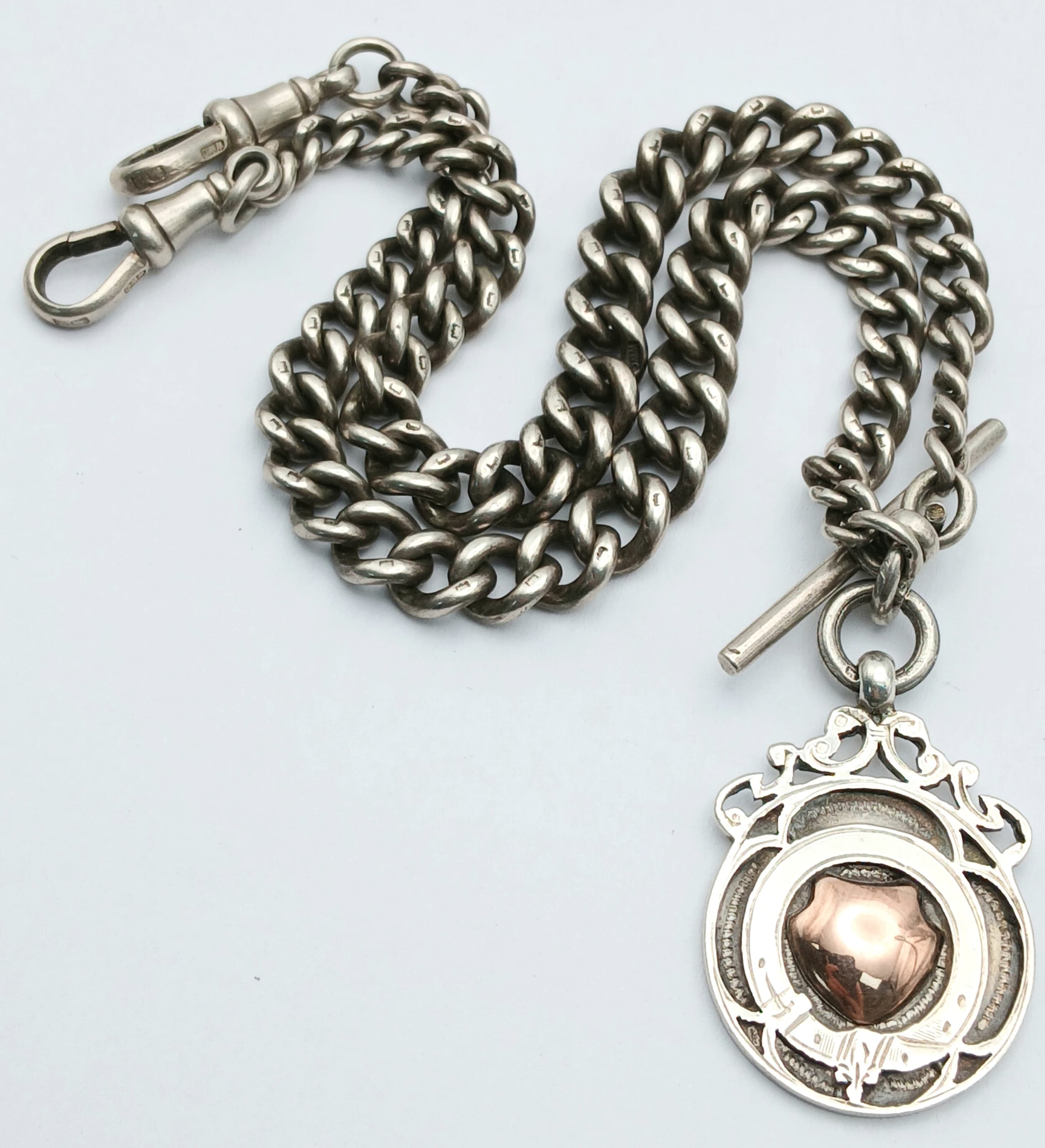 A Classic Antique Sterling Silver Albert Chain and Vintage Sterling Silver Fob with gold plated centre shield. 38cm length with twin lobster clasps and T-bar. 51.8g total weight.