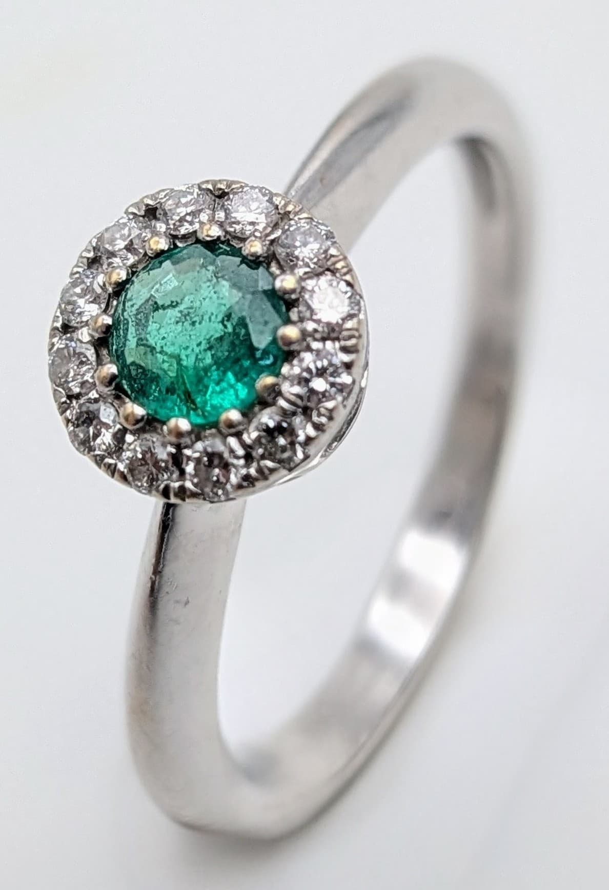 A 14K White Gold, Emerald and Diamond Ring. A round cut emerald with diamond halo. Size J. 2g total weight. MT3.