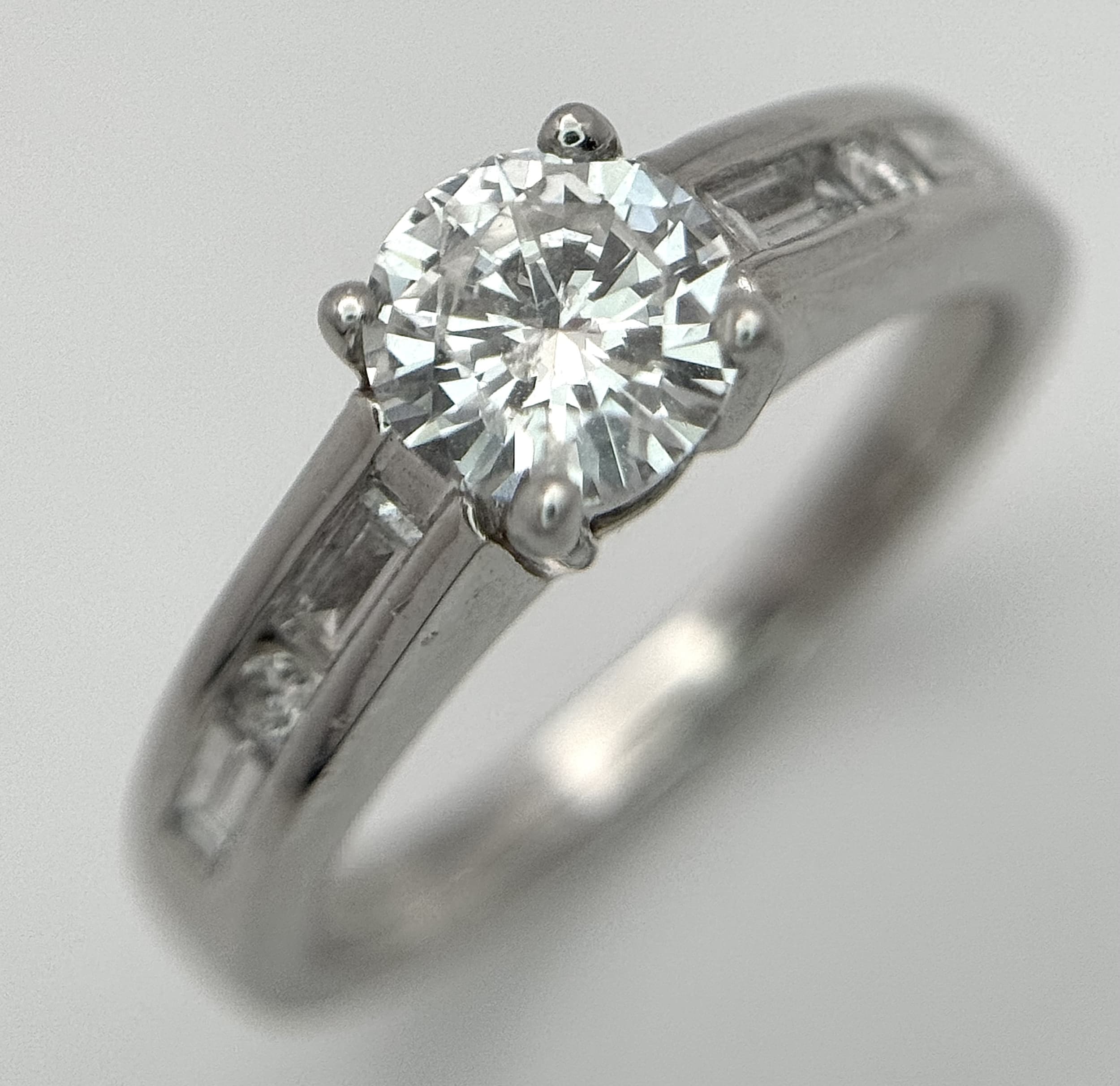 A Showstopping 950 Platinum Diamond Ring. A 0.71ct round brilliant cut centre stone, G colour and SI2 clarity, with 0.28ctw round brilliant cut and baguette cut diamonds on shoulders, H - I colour and SI1 clarity. Size M, 6.5g total weight. Comes with WGI certificate. Ref: NL00136/96509