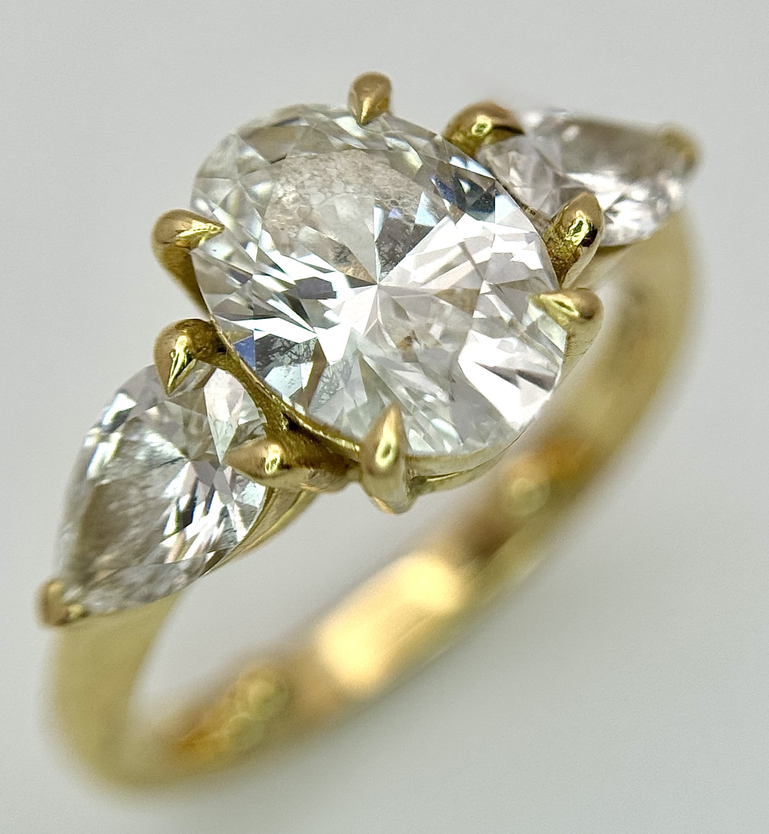An Eye-Catching 18K Yellow Gold Three Stone Lab-Grown Diamond Ring. A 1.5ct oval brilliant cut centre stone, D colour and VVS2 clarity, flanked by 0.80ctw pear brilliant cut lab-grown diamonds, E colour and VVS2 clarity. Ring has been resized to size G. 4.28g total weight. Each diamond comes with an IGI certificate. Ref: NL20/44506