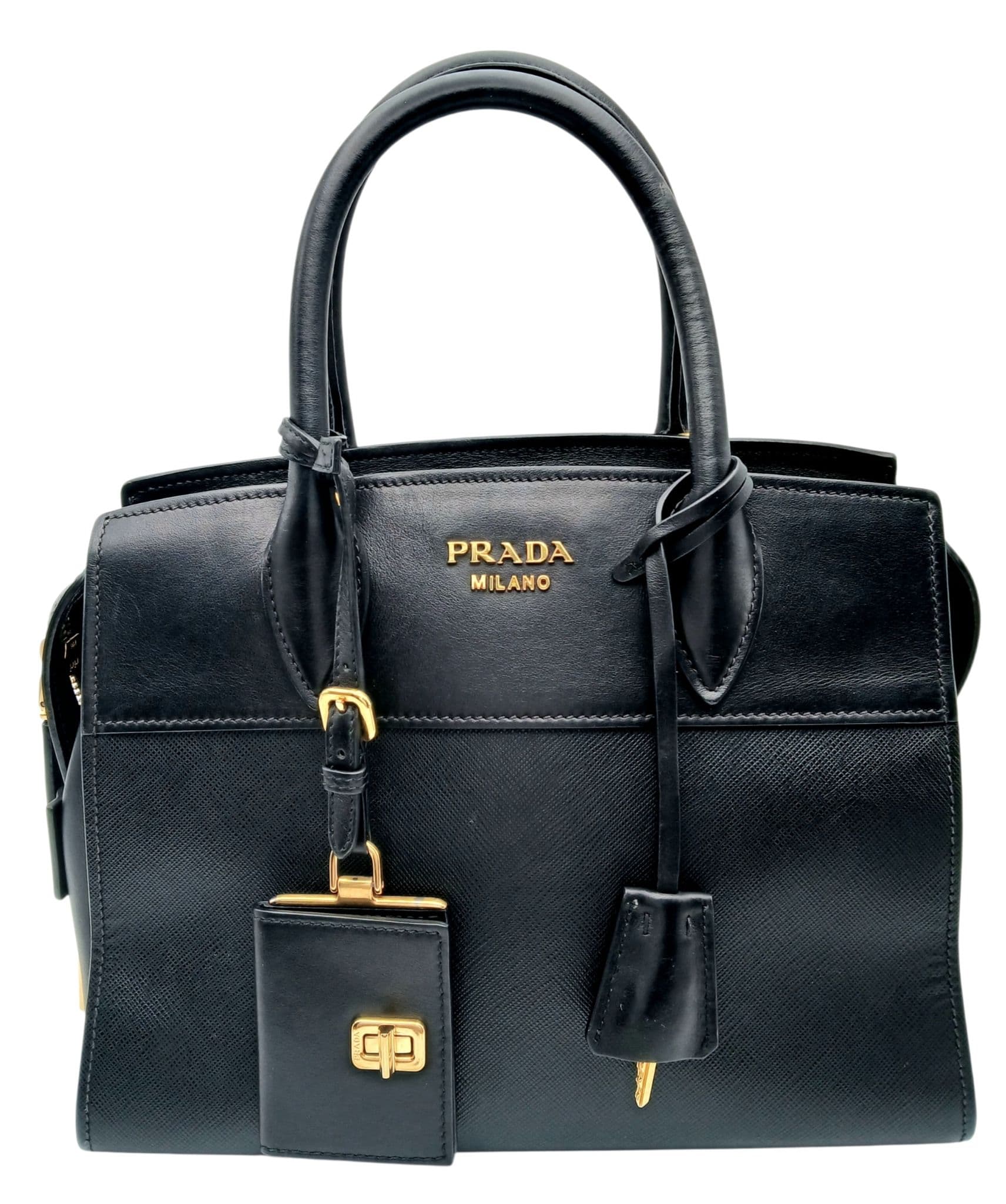 A Prada Black Saffiano Leather Tote Bag. Black Saffiano and smooth leather exterior with gold-toned hardware, dual rolled top handles, detachable clochette, keys, padlock and mini leather pouch. Features a zipped top closure. Black textile interior with one main compartment, two slip pockets and one zipped pocket. Approx 25cm length x 19cm height x 14cm depth. Some marks, scratches and signs of wear to the leather and hardware. Comes with a certificate of authenticity and a detachable shoulder strap. Please see photos or request a condition report. Ref: 28605.