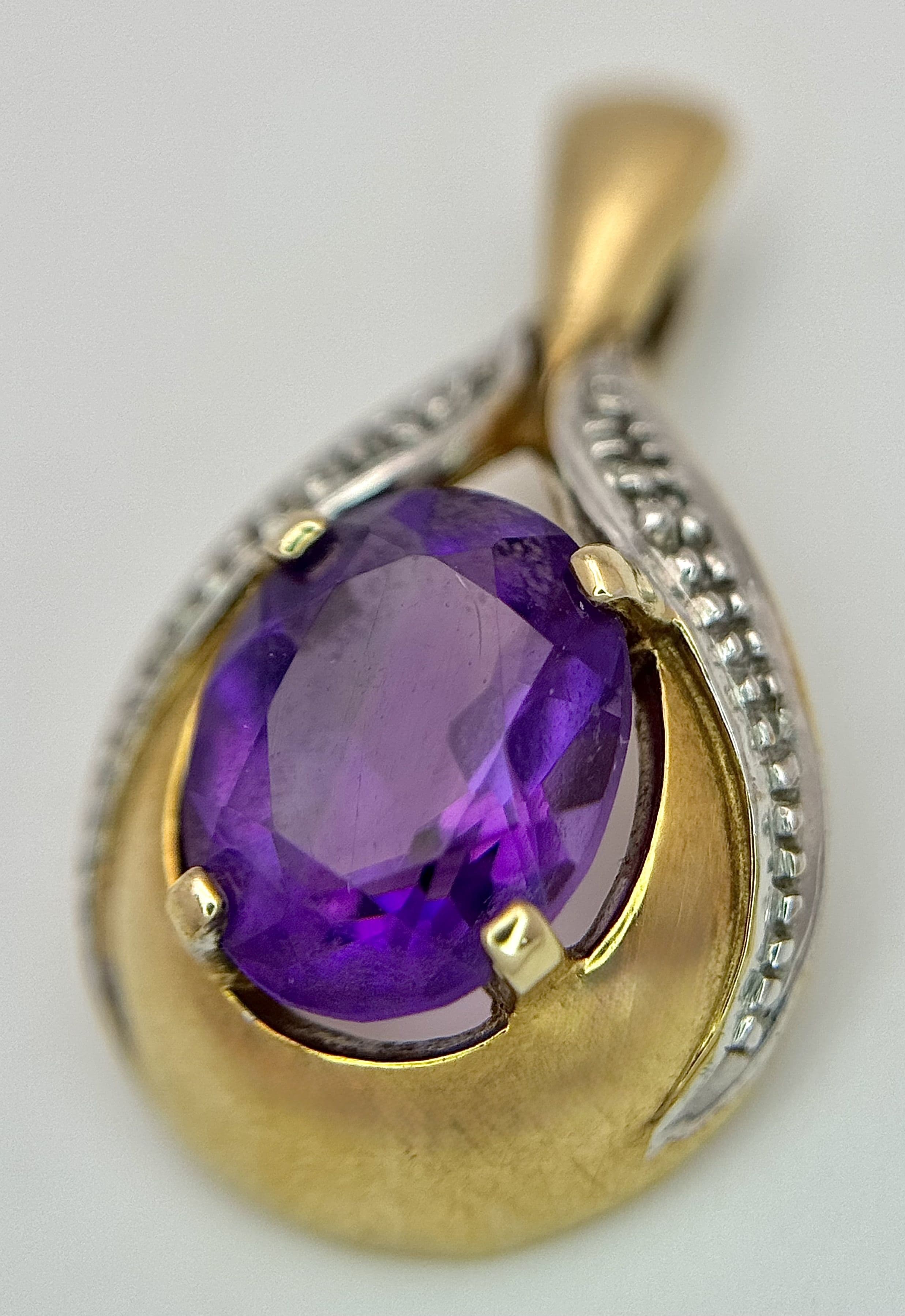 A 9K Yellow Gold Amethyst Pendant. White stone accents. 1.25ct oval cut amethyst. 2cm. 1.88g total weight.