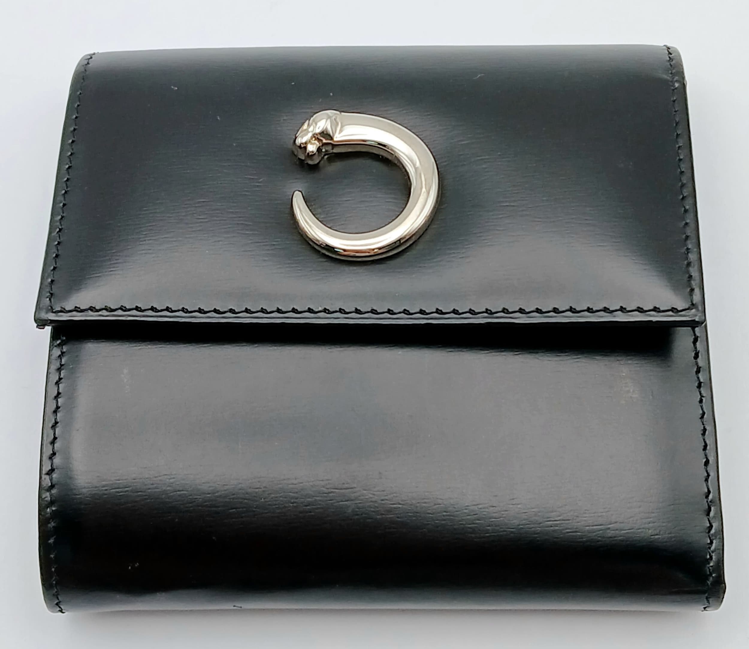 A Cartier Panthère Black Leather Compact Wallet. Black smooth leather exterior with silver-toned hardware and stud button closure. Black leather interior with multiple card slots, a note compartment, an open pocket and a press-stud coin pocket. Approx 9cm length x 10cm height when folded. Some marks, scratches and signs of wear to the leather. Please see photos or request a condition report. Ref: 28692.