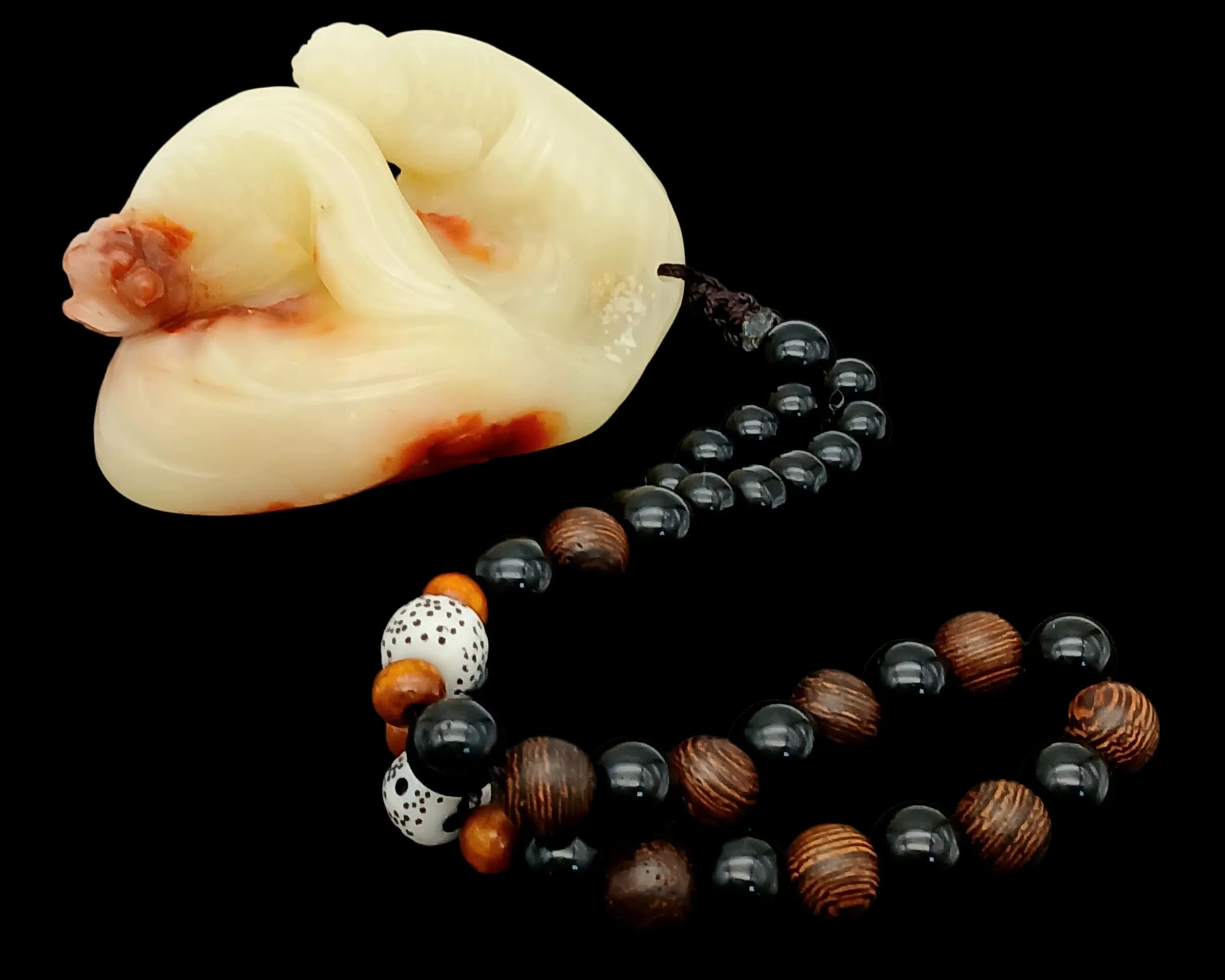 Chinese Shoushan jade Stone (寿山石) Carving with Beaded Necklace.A polished Shoushan stone carving from Fujian, featuring a smooth, semi-translucent body with natural russet inclusions and soft flowing contours. Accompanied by a handcrafted mixed-material beaded necklace, including black polished beads, wood-grain beads, and speckled accent beads.Colour: Cream-white with natural russet tones.Dimensions:Pendant: approx. 15 cm.Come with box