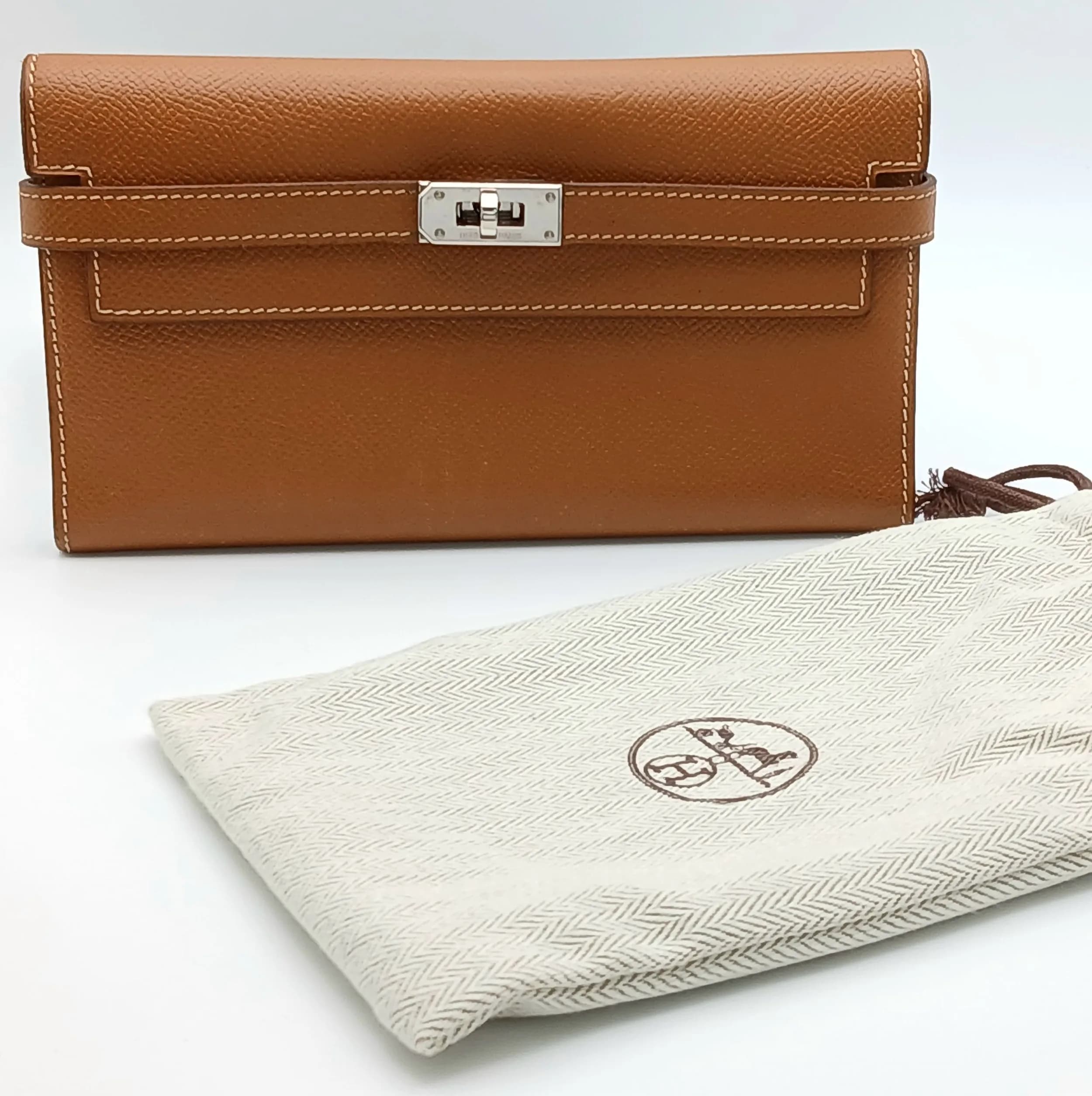 An Hermès Tan Epsom Leather Kelly Long Wallet. Tan Epsom leather exterior with silver-toned hardware, front strap detail and signature Kelly turn-lock closure. Matching leather interior with multiple card slots, open compartments and a central zipped coin pocket. Approx 19cm length x 12cm height (when folded). Light signs of wear and tiny scratches to the leather and hardware but in good condition overall. Comes with a certificate of authenticity and dust cover. Please see photos or request a condition report. Ref: 28708.