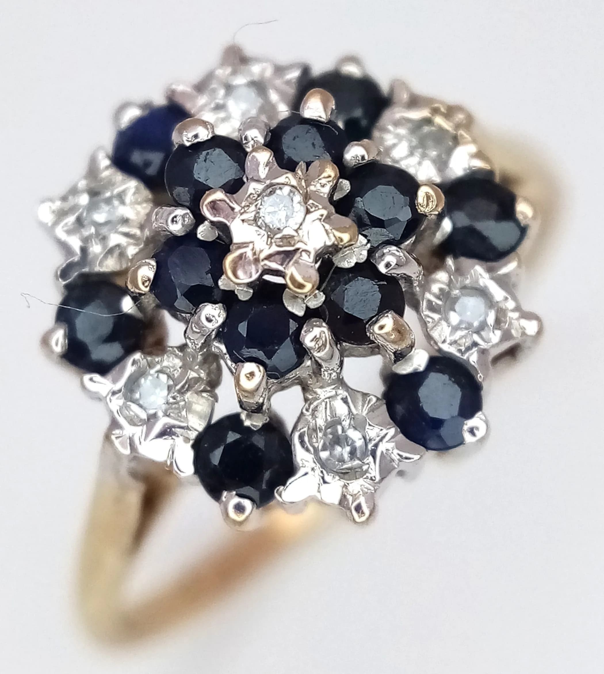 An Elegant 9k Yellow Gold Diamond and Sapphire Cluster Ring. Size M1/2. The Diamonds and Sapphires are tier mounted making up a Crown size of 1.2cm. The Ring has a gross weight of 2.5 grams.