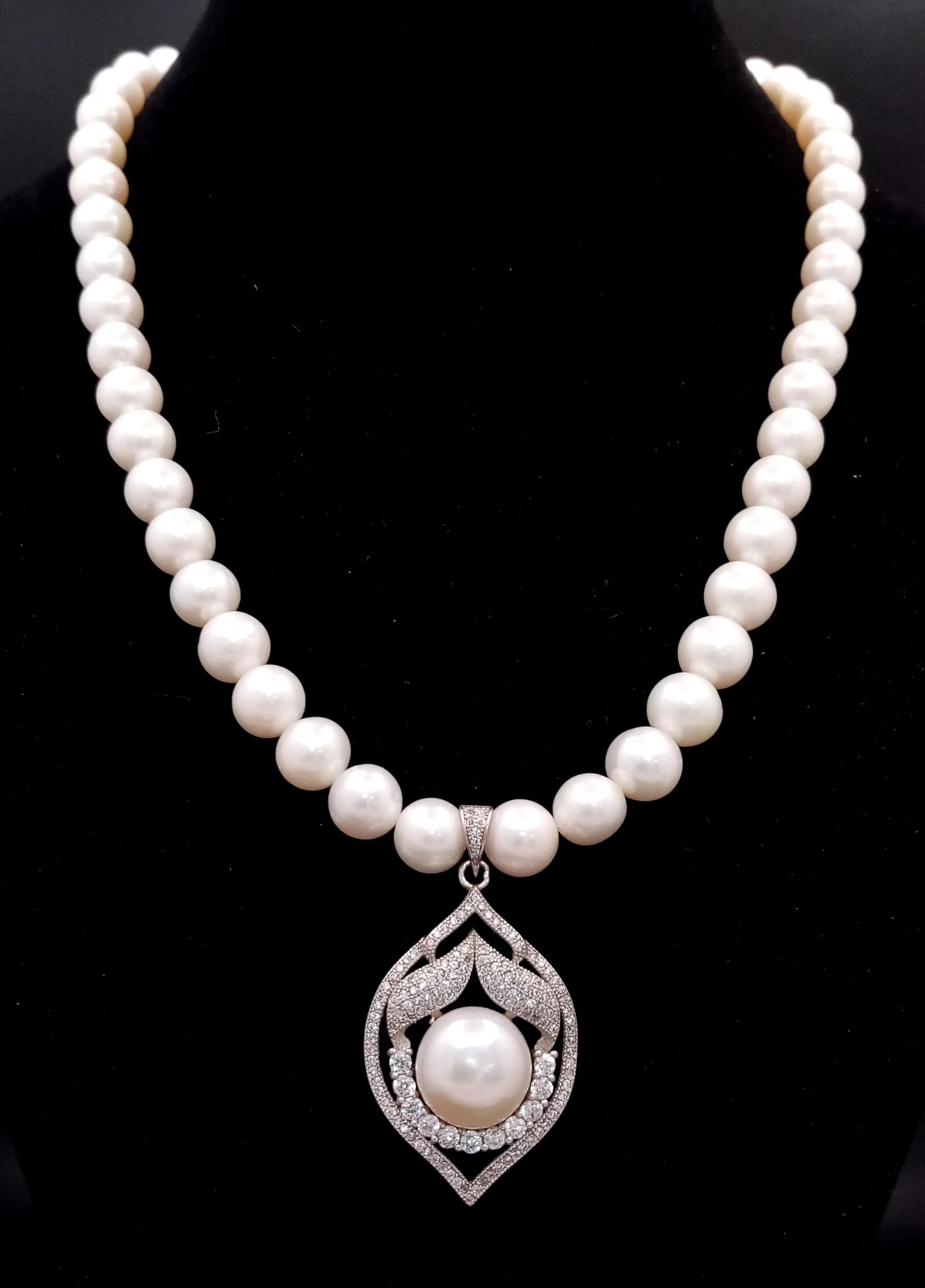 An elegant Freshwater Pearl Necklace with Silver Pearl and Stone Set Pendant. Approx 42cm in length, strung with cream freshwater pearls and fitted with a decorative silver floral clasp. The necklace features a silver openwork pendant set with a central pearl and clear stone accents. Please see photos for details.