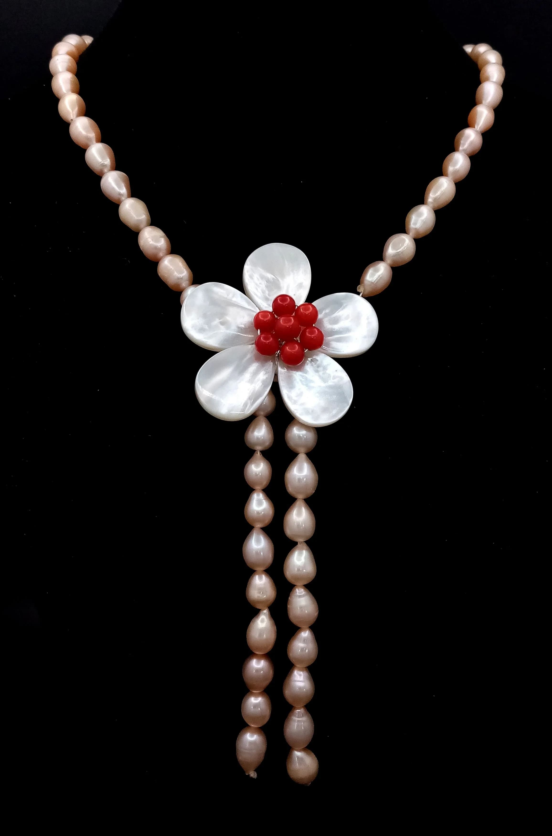 A pretty Freshwater Pearl and Mother of Pearl Flower Pendant Necklace. Approx 43cm in length, strung with peach-tone freshwater pearls. The necklace features a mother of pearl floral pendant with red coral beads to the centre and pearl drop tassel detail. Please see photos for details.