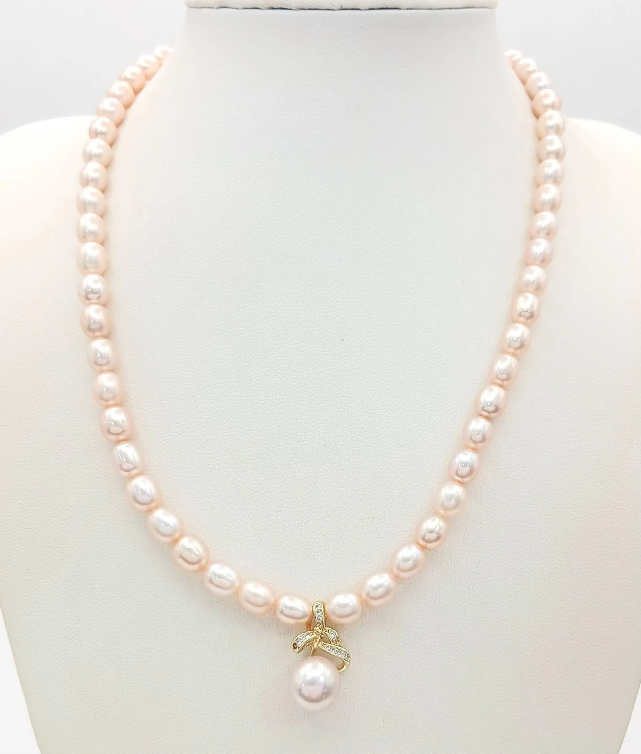 A Lovely Freshwater Pearl Necklace with Pearl and Crystal Set Pendant. Approx 42cm in length, strung with soft pink/cream freshwater pearls, pearl drop and clear stone bow detail. Please see photos for details.