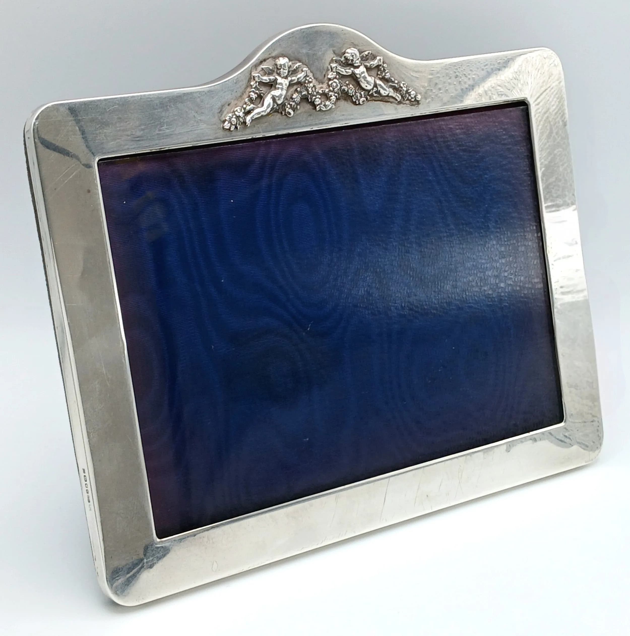 A Vintage London Hallmarked Silver Photograph Frame. Rectangular form with polished silver border and decorative cherub detail to one side. London hallmarked silver. Overall approx 21.5cm x 16.5cm. Silver frame border approx 16.5cm x 2cm x 0.7cm. Total weight 433 grams.