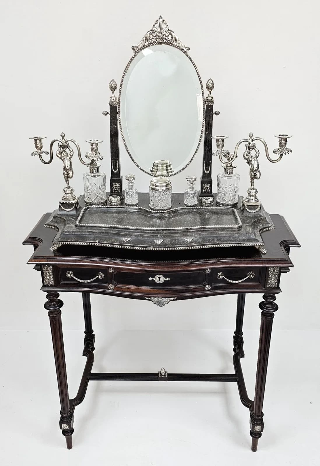 A RARE BEAUTIFUL WOOD AND SOLID SILVER PORTUGESE VANITY TABLE (CIRCA 1860) ALL TRIMMINGS BEING SILVER INCLUDING THE ACORN ON THE BASE WITH FABULOUS DECORATIVE HANDLES, INCLUDED WITH THIS TABLE ARE A PAIR OF STUNNING CANDALABRAS, CRYSTAL AND SILVER TOPPED BOTTLES AND ON OPENING THE DRAWER YOU WILL FIND A SILVER MANICURE SET WITH ITS OWN MIRROR. THE MAIN MIRROR ATTACHED TO THE DRESSING TABLE IS OVAL SHAPED WITH DECORATIVE TRIM WITH 2 FURTHER ACORNSHAPED FINIALS EITHER SIDE OF THE MIRROR. MANY PARTS ARE HALLMARKED AND WE WOULD ESTIMATE THE SILVER WEIGHING 4.5 - 5 KILOS. THE WHOLE SET IS IN FANTASTIC CONDITION. WINNING BIDDER MUST COLLECT FROM CADMORE HQ DUE TO THE SIZE, WEIGHT AND FRAGILITY.