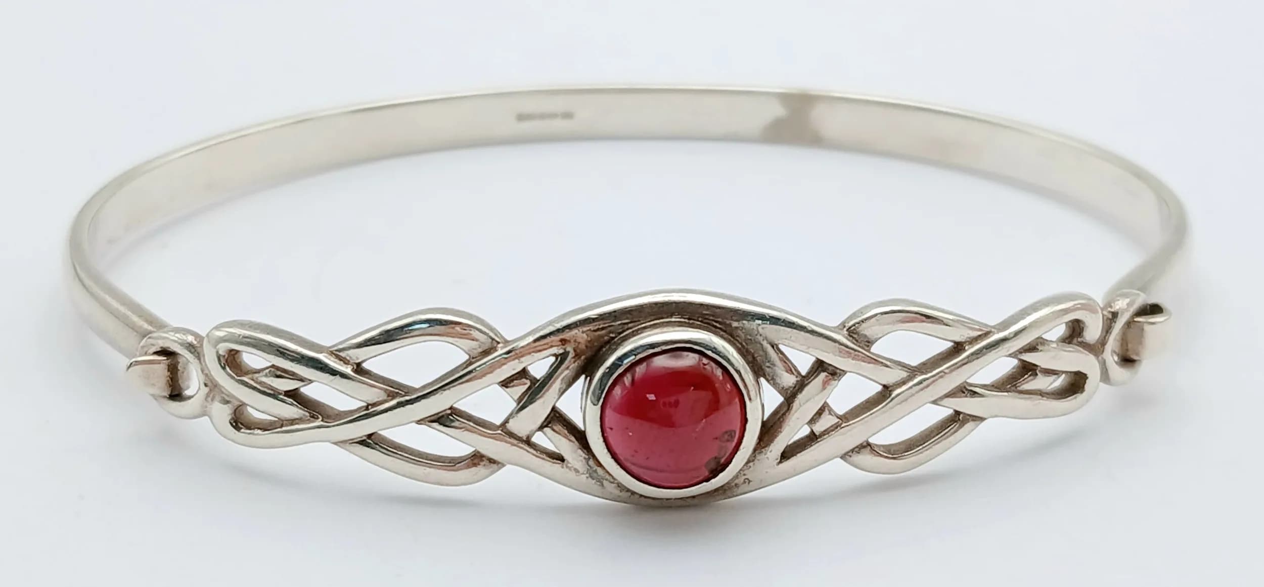 A STERLING SILVER, RED STONE SET, CELTIC DESIGN BANGLE. 14.1G. SC 5139