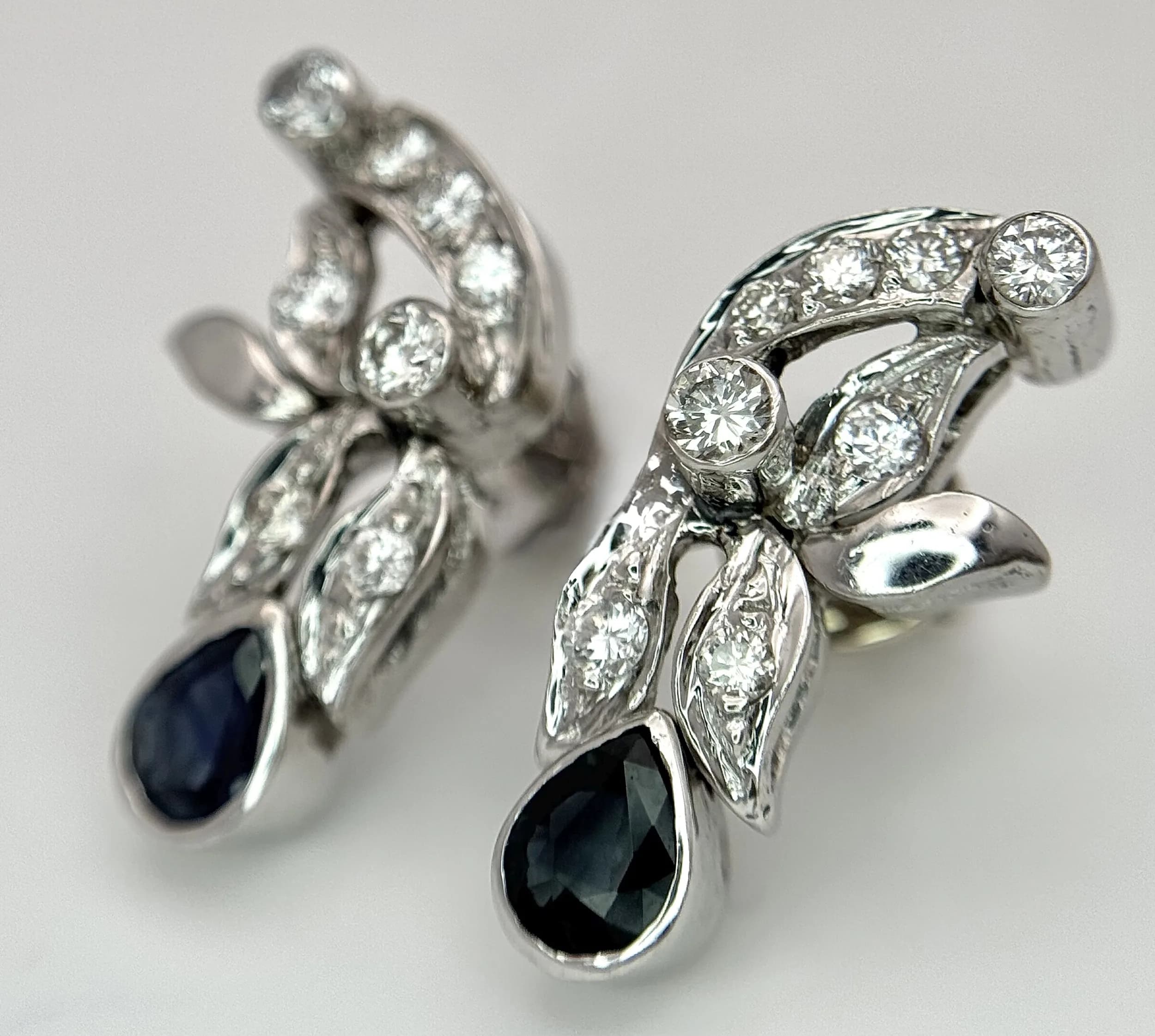 A Pair of Victorian Style 18K White Gold, Diamond and Sapphire Drop Earrings. Abstract floral form that ends with sapphire teardrops. 2.5cm. c.1ctw of diamonds having G colour and VS2 clarity. 7.4g total weight. MT34.