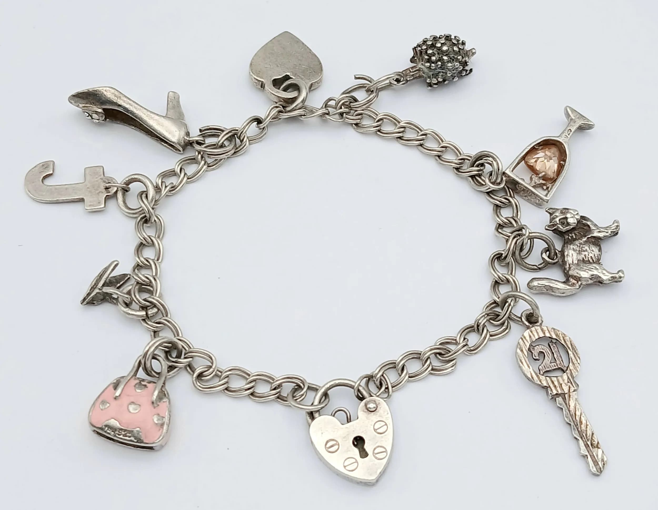 A Vintage Silver Charm Bracelet. Set with various novelty charms including heart padlocks, key, cat, horse, bag and other decorative charms. Approx 16cm length. Total weight 18.91 grams.