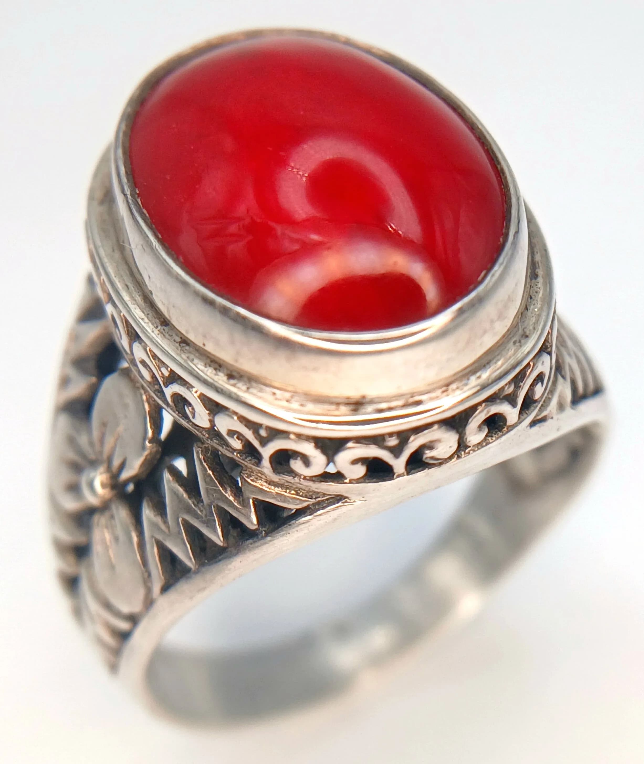 A Unique Vintage Sterling Silver and Red Coral Ring. Size N. The Ring is set with a 1.5cm Red Coral Cabochon with the upper half of the ring being highly detailed. Gross weight 5.93 grams.