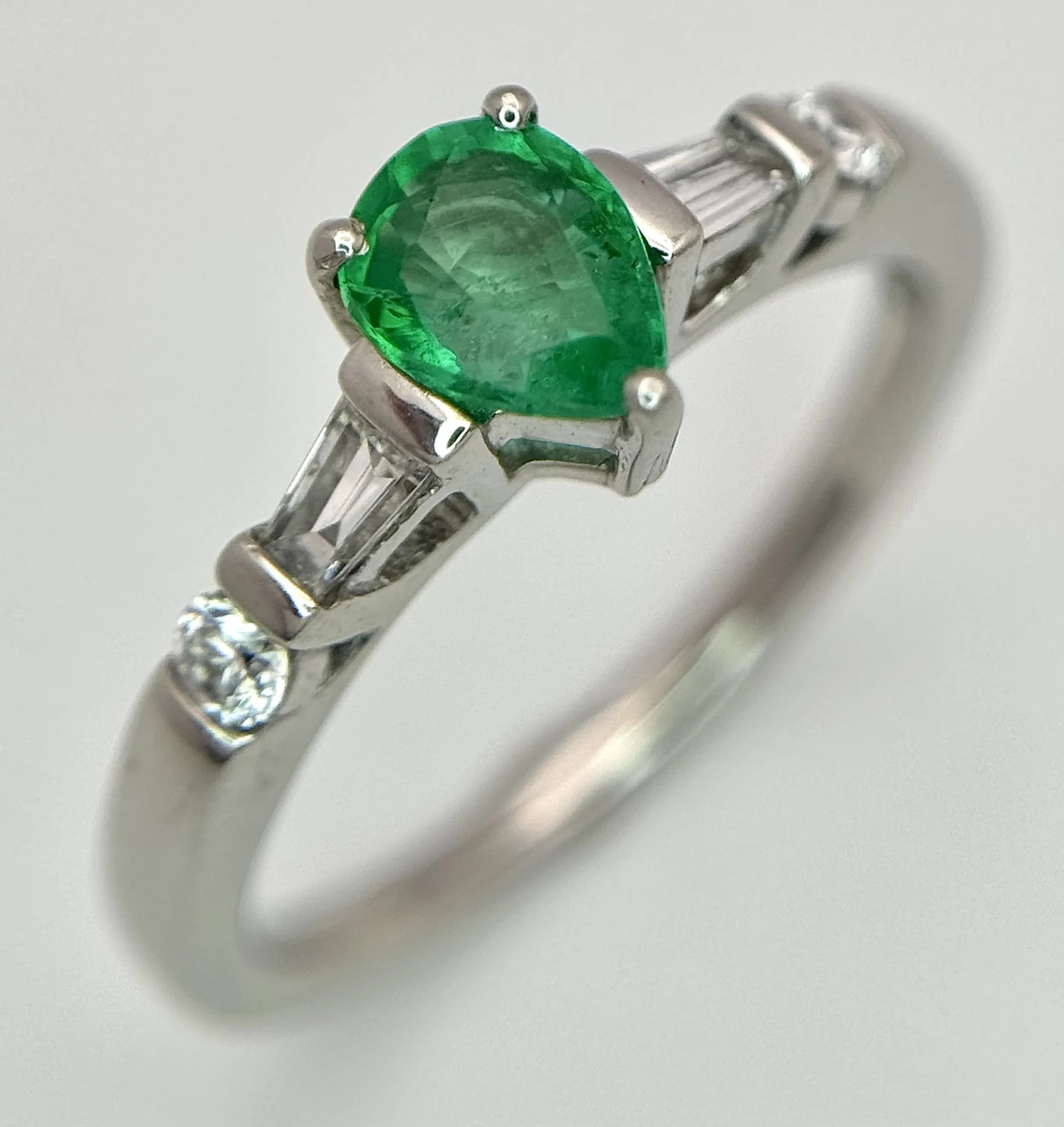 A 950 Platinum, Emerald and Diamond Cocktail Ring. 0.40ct pear-shaped emerald flanked by tapered baguette and round brilliant cut diamonds. Size M 1/2. 4.9g total weight. MT23.