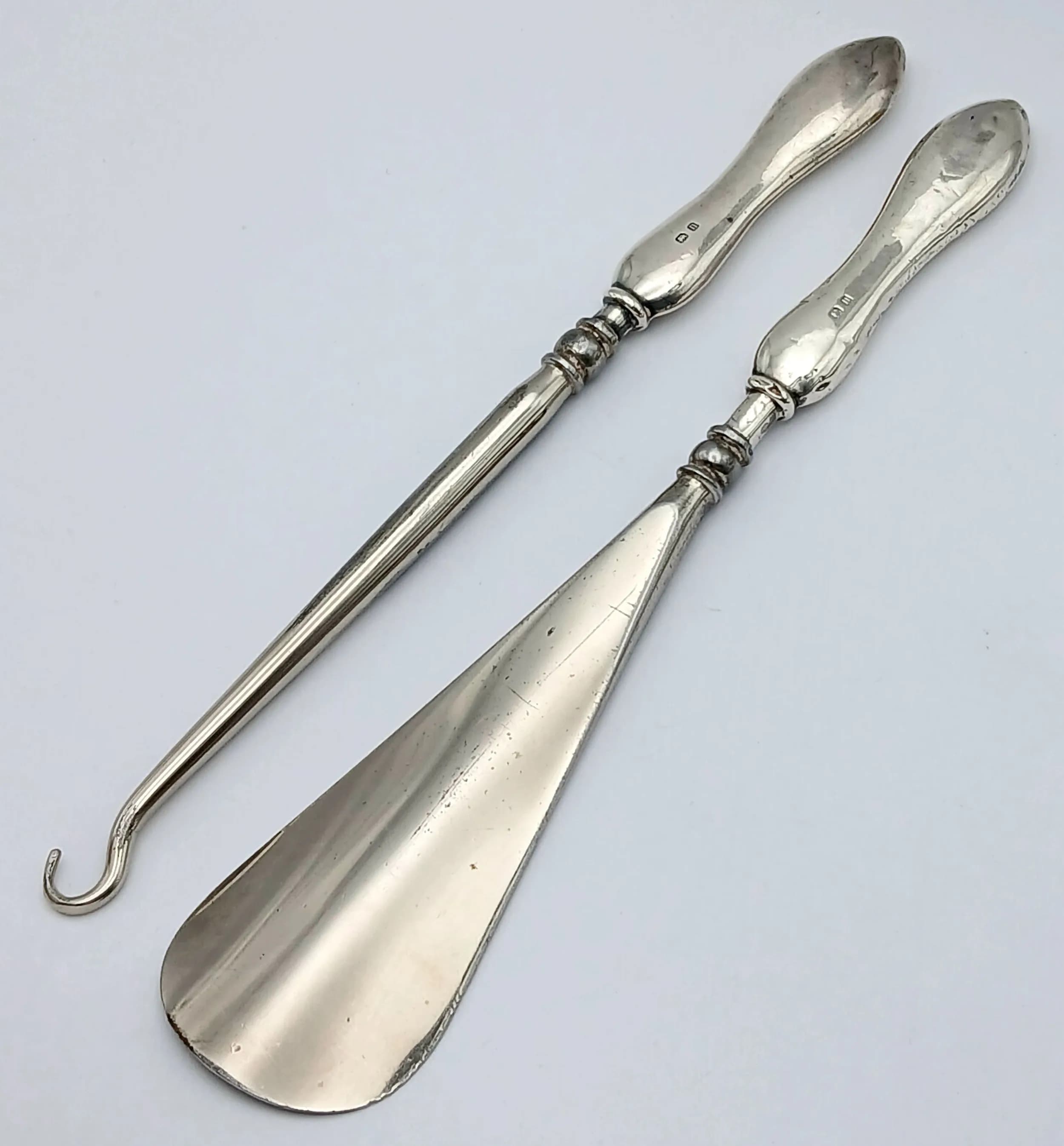 A Pair of Antique Sterling Silver Accessories. Comprising a silver crochet hook/wool tool and a silver shoe horn, each with shaped silver handle. 1912 Birmingham hallmarked. Approx 17cm length. Total weight 70.4 grams.