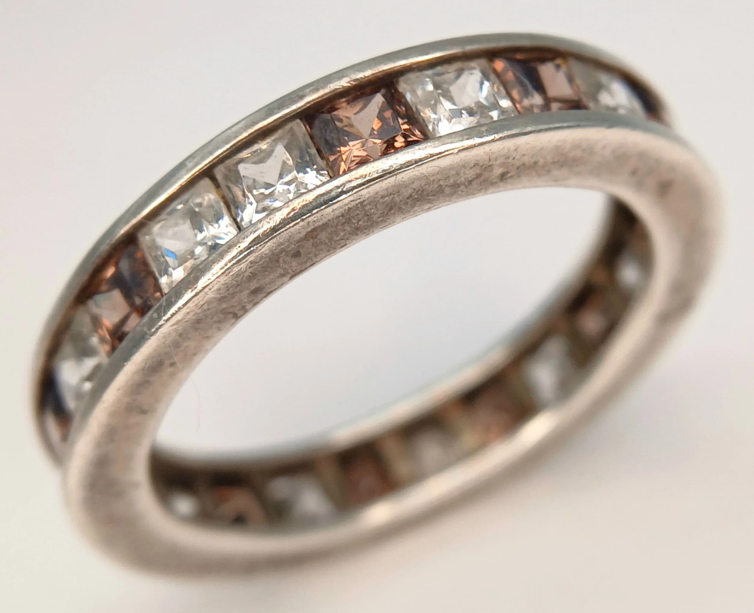 An Attractive 925 Silver CZ Stone Set Eternity Ring. Channel set with small square cut CZ stones in a polished silver band. Ring size R. Approx 4mm band width. Total weight 4.5 grams.