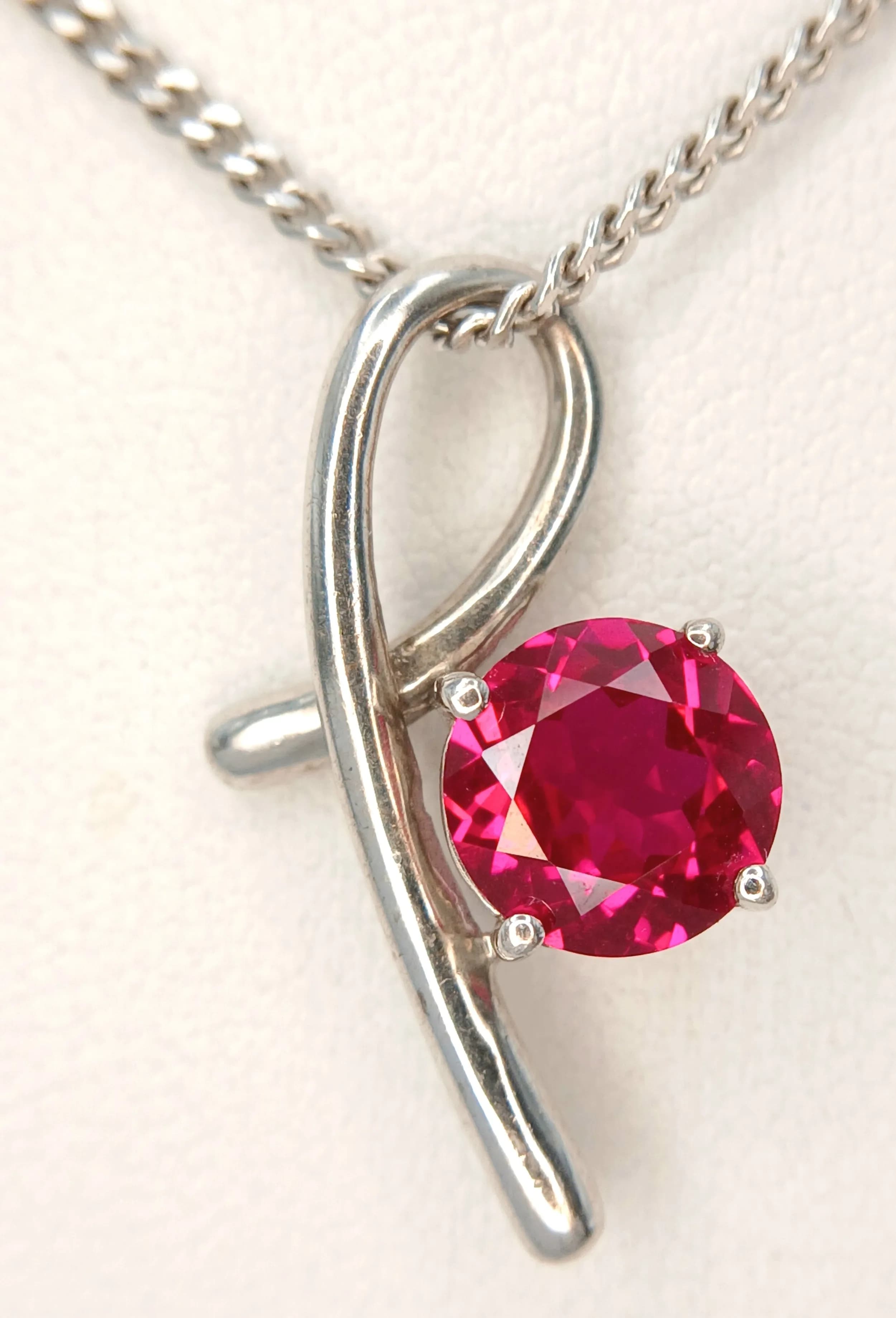 A Delightful 925 Sterling Silver Pink Stone Set Ribbon Pendant Necklace-44cm Length Chain. The Pendant is set with a 7mm Round Cut Pink Stone and measures 3cm Drop. Total weight: 5.78g.