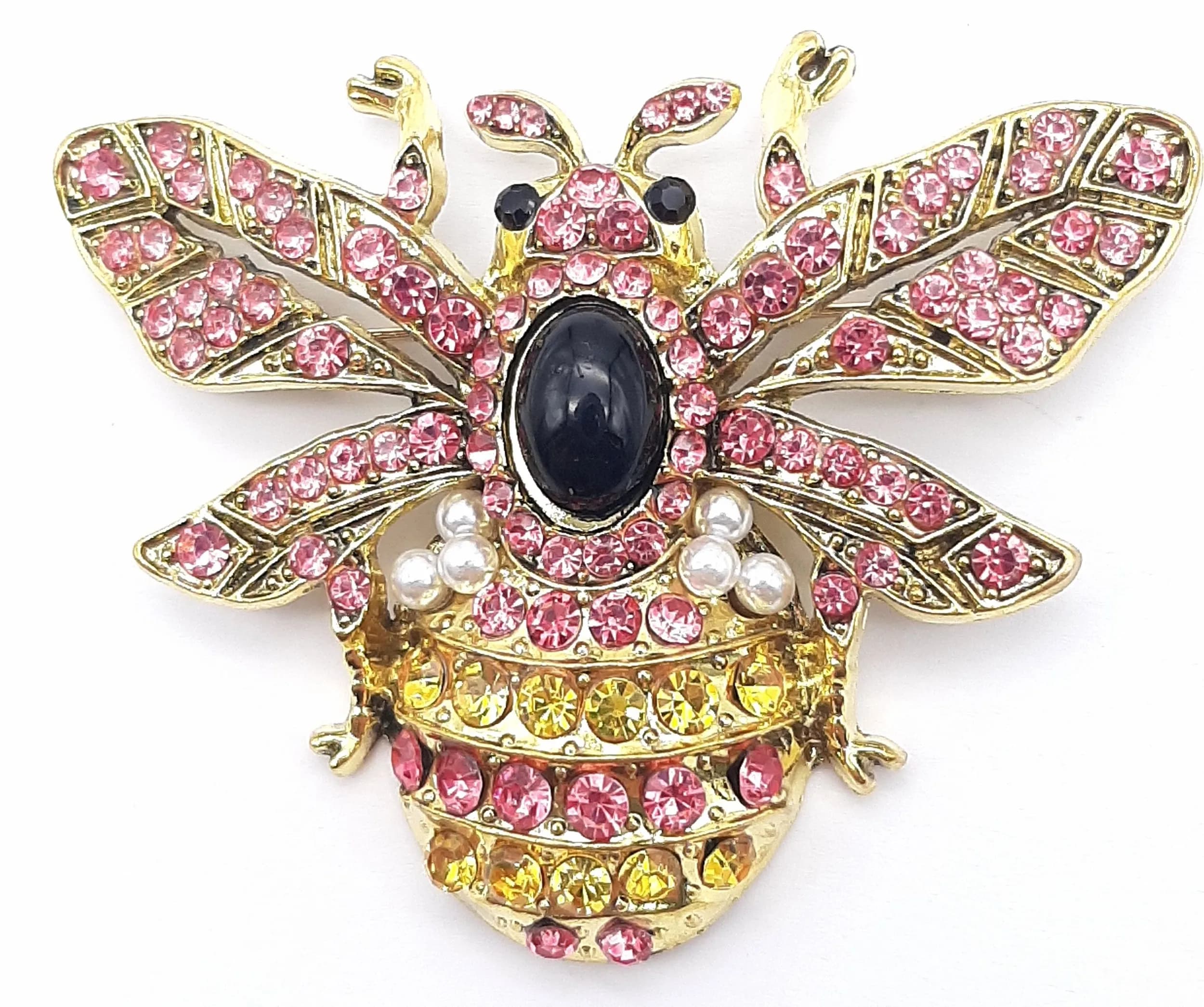 A Decorative Stone Set Bee Brooch. Gold-tone metal bee brooch set with pink and yellow rhinestones, faux pearl accents, black stone-effect eyes and a black oval cabochon body. Measures approx. 6cm x 8cm.