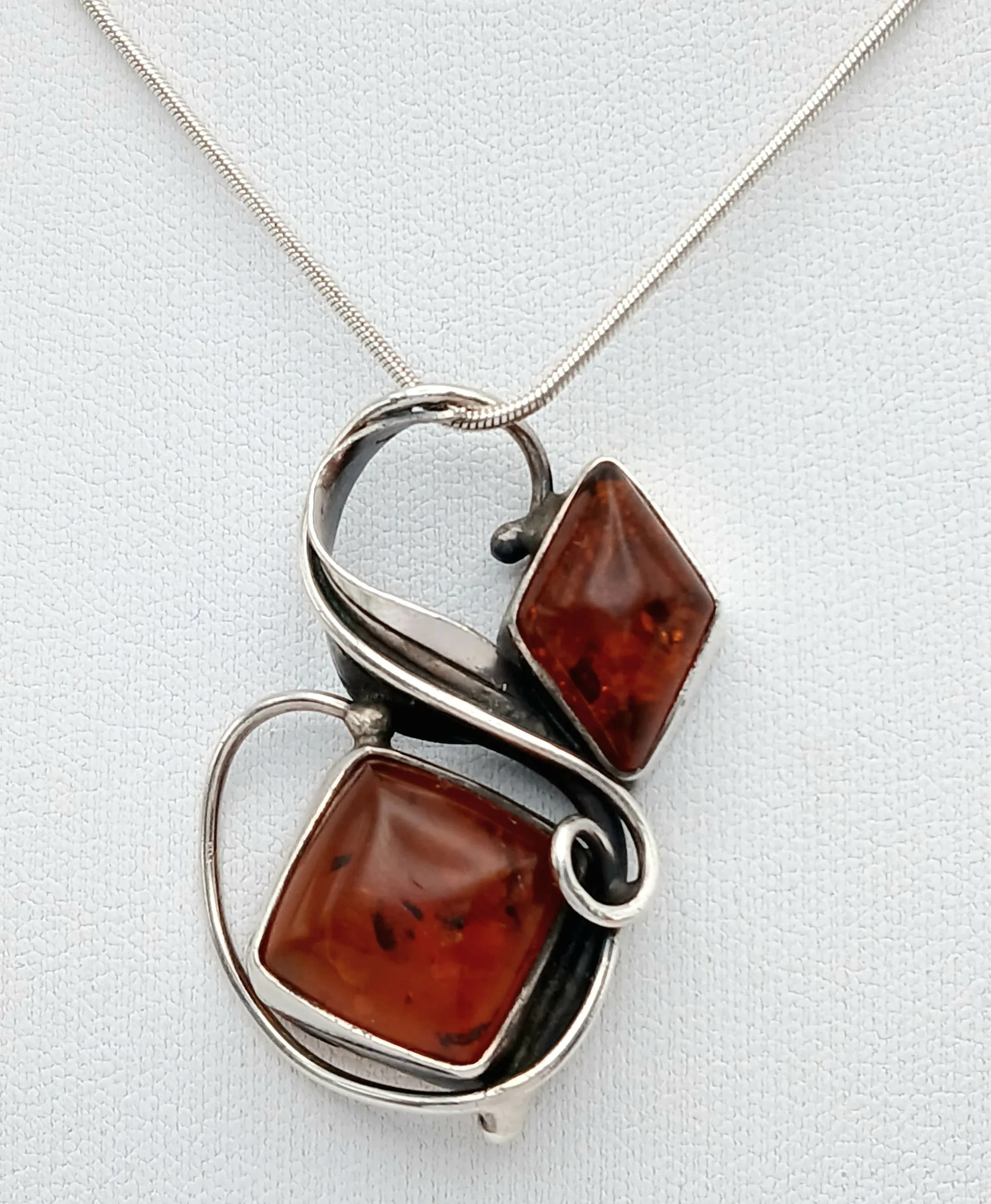 A Lovely 925 Silver Amber Set Pendant Necklace. Set with two cognac amber cabochons in a polished silver swirl design pendant. Chain approx 40cm length. Pendant approx 4cm x 3cm. Total weight 12.14 grams.