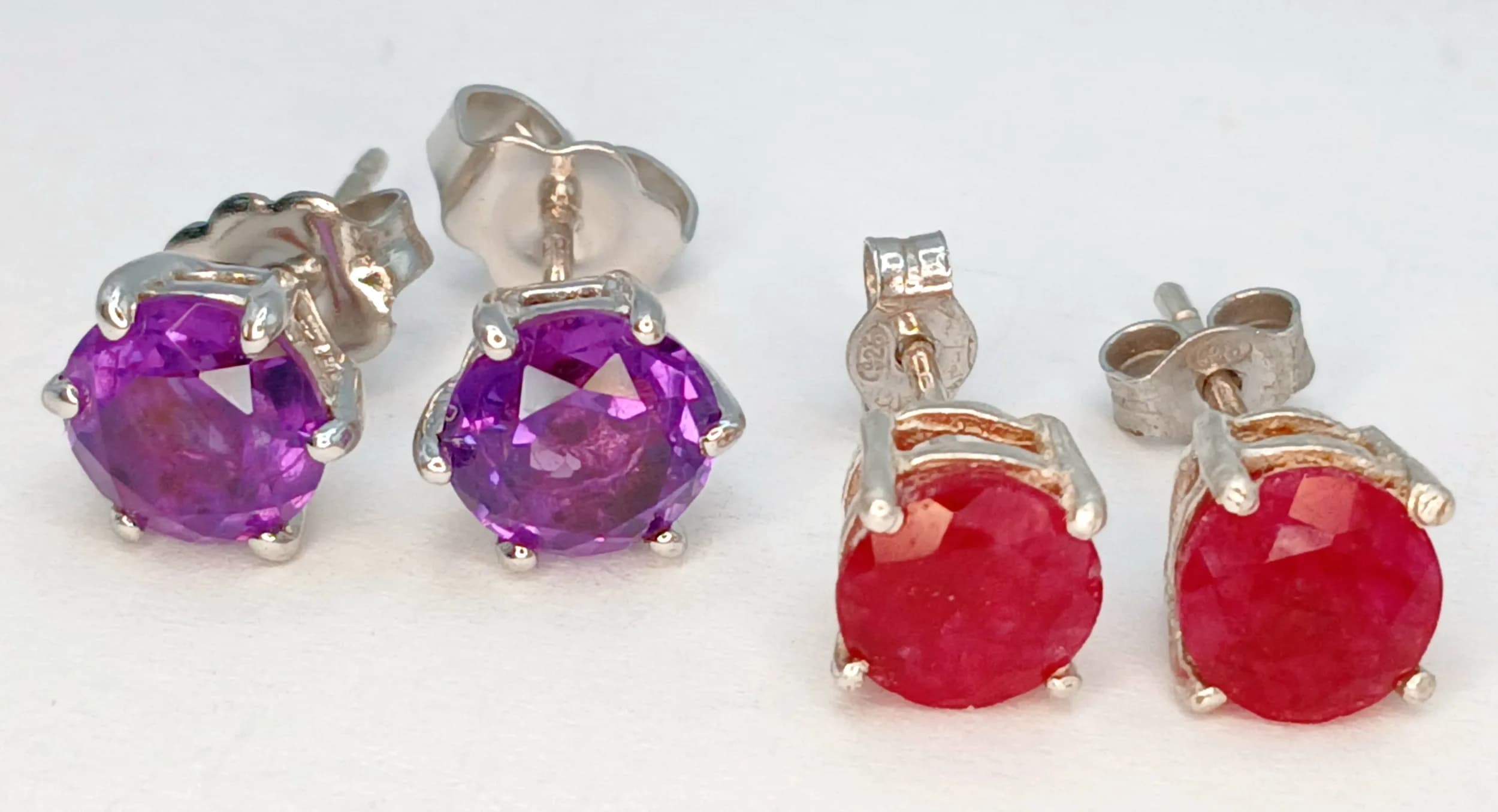 Two Pairs of 925 Sterling Silver Amethyst and Ruby Stud Earrings. Comprising a pair set with round faceted amethysts and a pair set with round cabochon rubies, in claw settings with post and butterfly fittings. Each stone measures 0.6cm diameter. Gross weight 2.93 grams.
