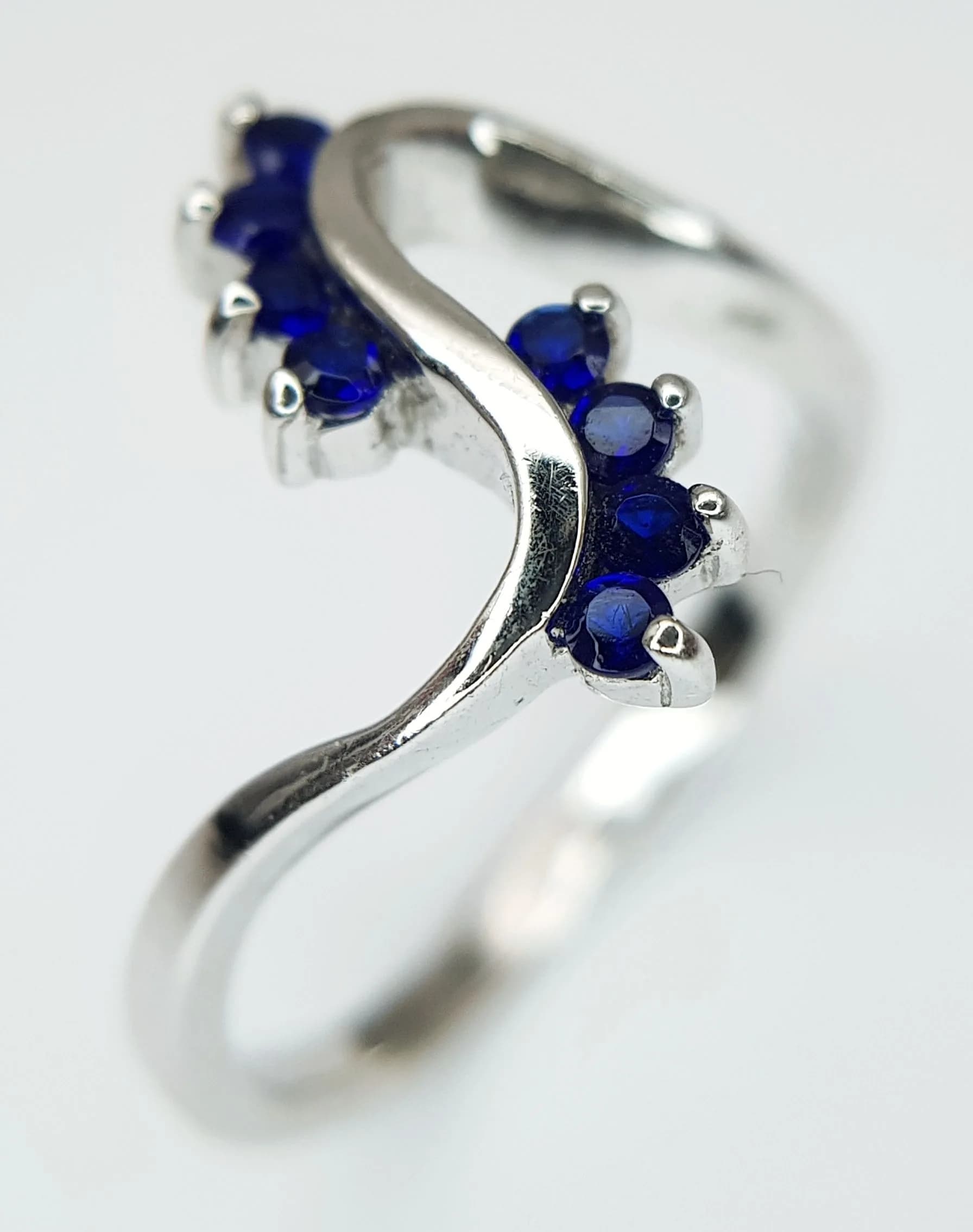 A Beautiful 925 Silver Blue Stone Swirl Ring. Size R. Features an openwork crossover design set with small round blue stones. Gross weight 2.95 grams.
