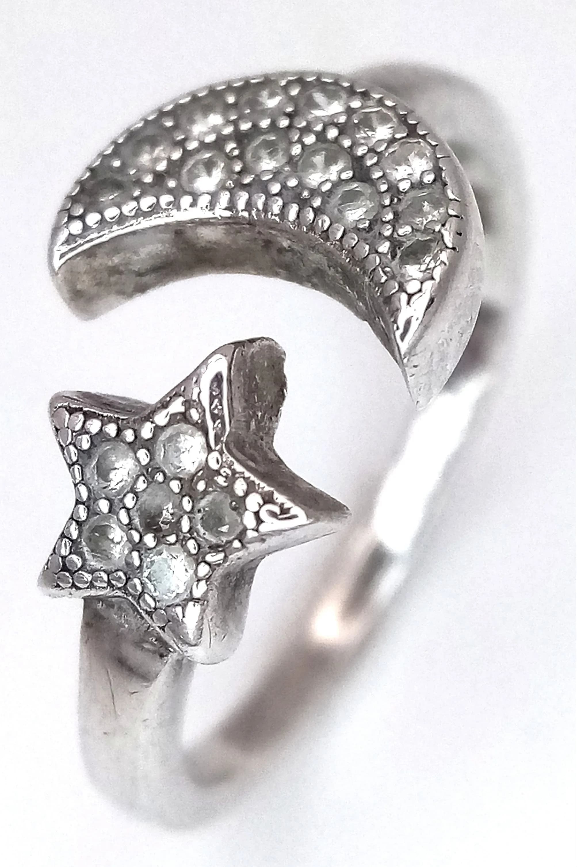 A Pretty 925 Silver CZ Set Moon and Star Adjustable Ring. Adjustable up to size D. Features a crescent moon and star design set with small CZ stones. Gross weight 1.4 grams.