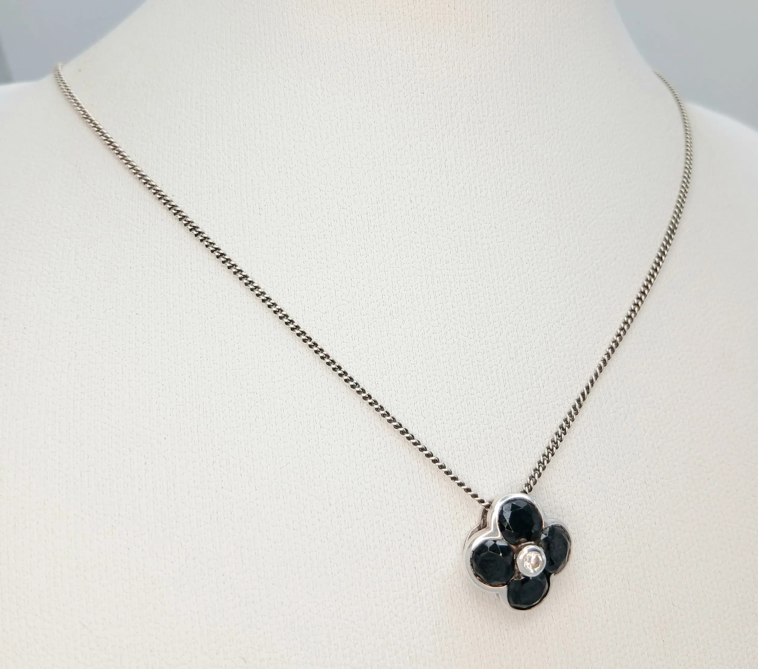 A Pretty 925 Sterling Silver Black Onyx and CZ Set Flower Pendant Necklace - 39cm Length. Features a four-petal black onyx flower pendant with a central CZ stone on a fine silver chain. The pendant measures 1.4cm x 1.4cm. Gross weight 4.07 grams.
