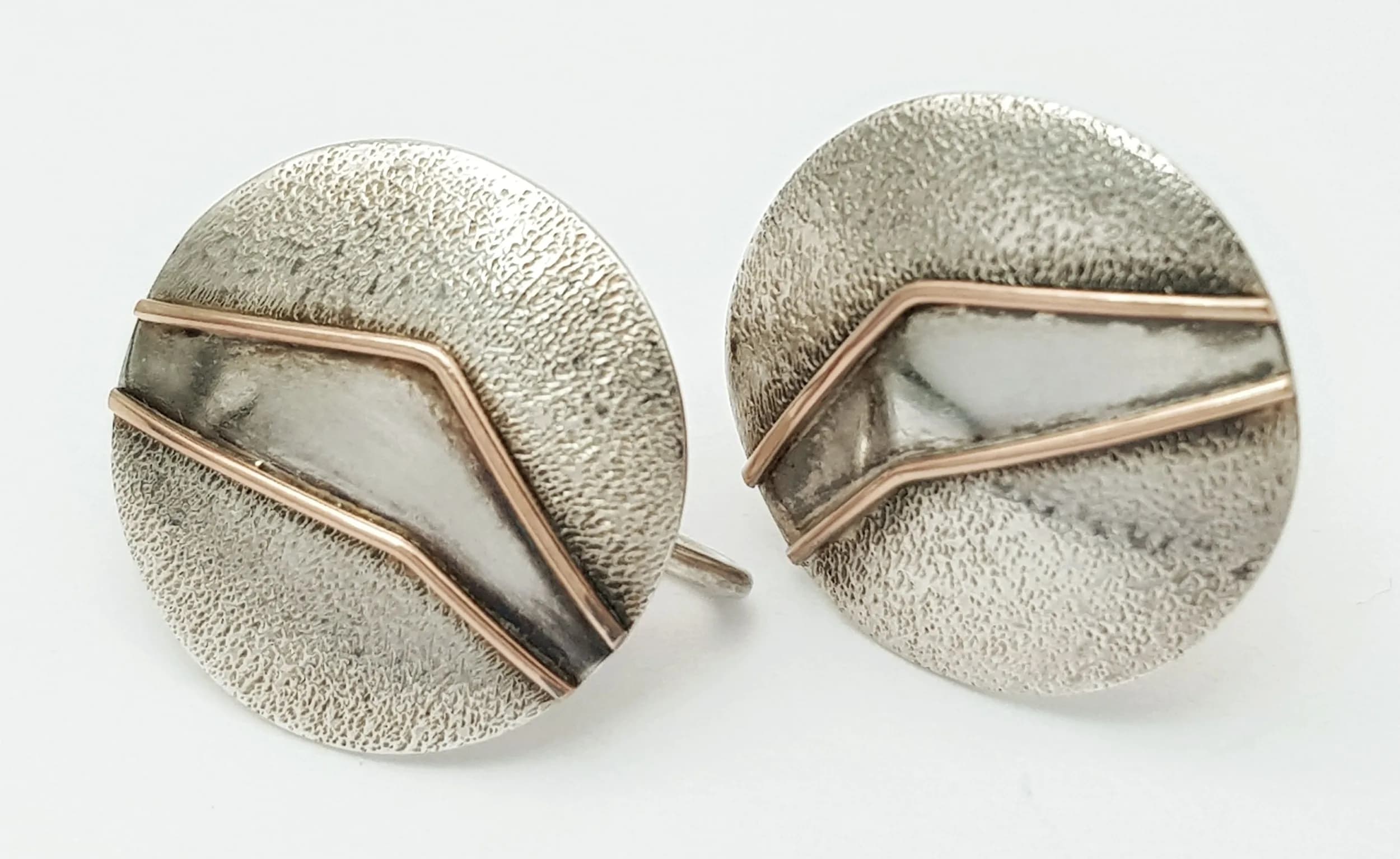 A Stylish Pair of Vintage Silver Two-Tone Circular Clip-On Earrings. Features textured circular fronts with polished silver and rose gold-toned chevron details, with screw-back fittings. Each earring measures 1.5cm diameter. Gross weight 2.75 grams.