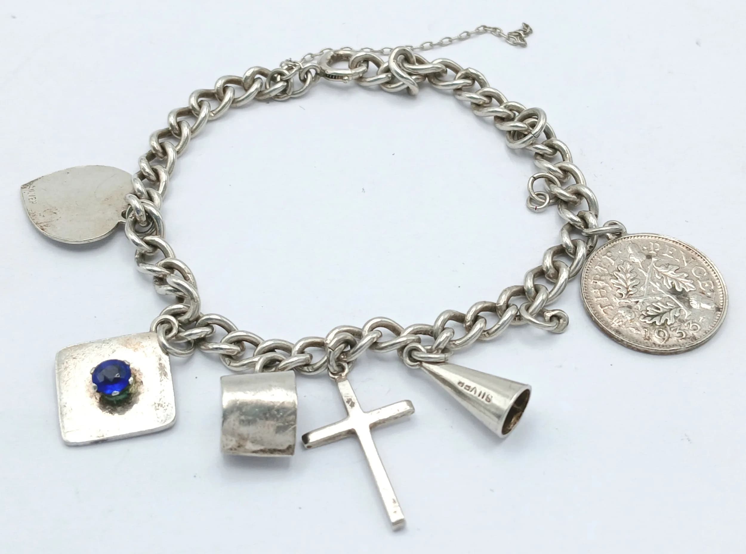 A Lovely Vintage Silver Multi-Charm Bracelet-20cm Length including Extender Chain. The Bracelet is hung with Cross, Coin, Horn, Heart and Square Sapphire Set Charms. Gross weight 13.42 grams.
