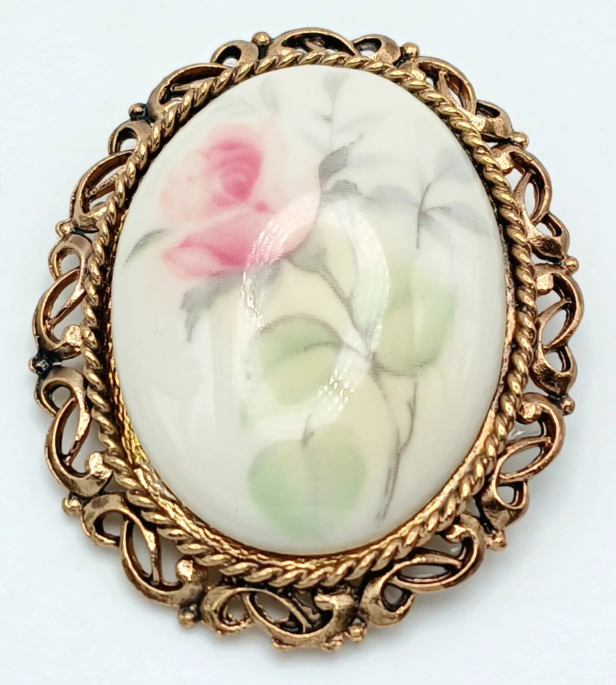 A vintage Donegal Parian China Floral Brooch. Oval ceramic panel with hand-painted rose detail in an ornate gold-tone frame. Approx 5cm x 4cm. Comes with original presentation box.