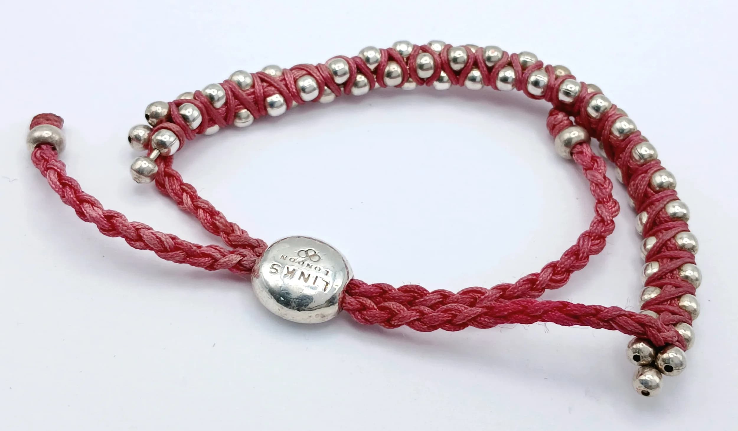 A Links of London 925 silver bracelet. Features a signature Effervescence design with a pink woven cord and adjustable toggle fastening. Total weight 21.86g. Approx 28cm length. Please see photos for details.