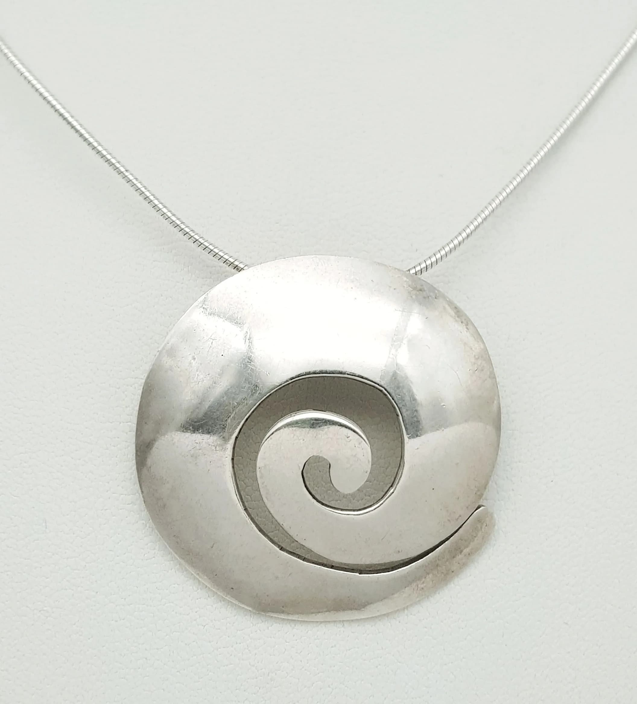 A Pretty 950 Silver Swirl Pendant Necklace. Featuring a 950 polished circular swirl pendant on a fine silver chain. Chain approx 40cm length. Pendant approx 3.5cm diameter. Gross weight 11.38 grams.