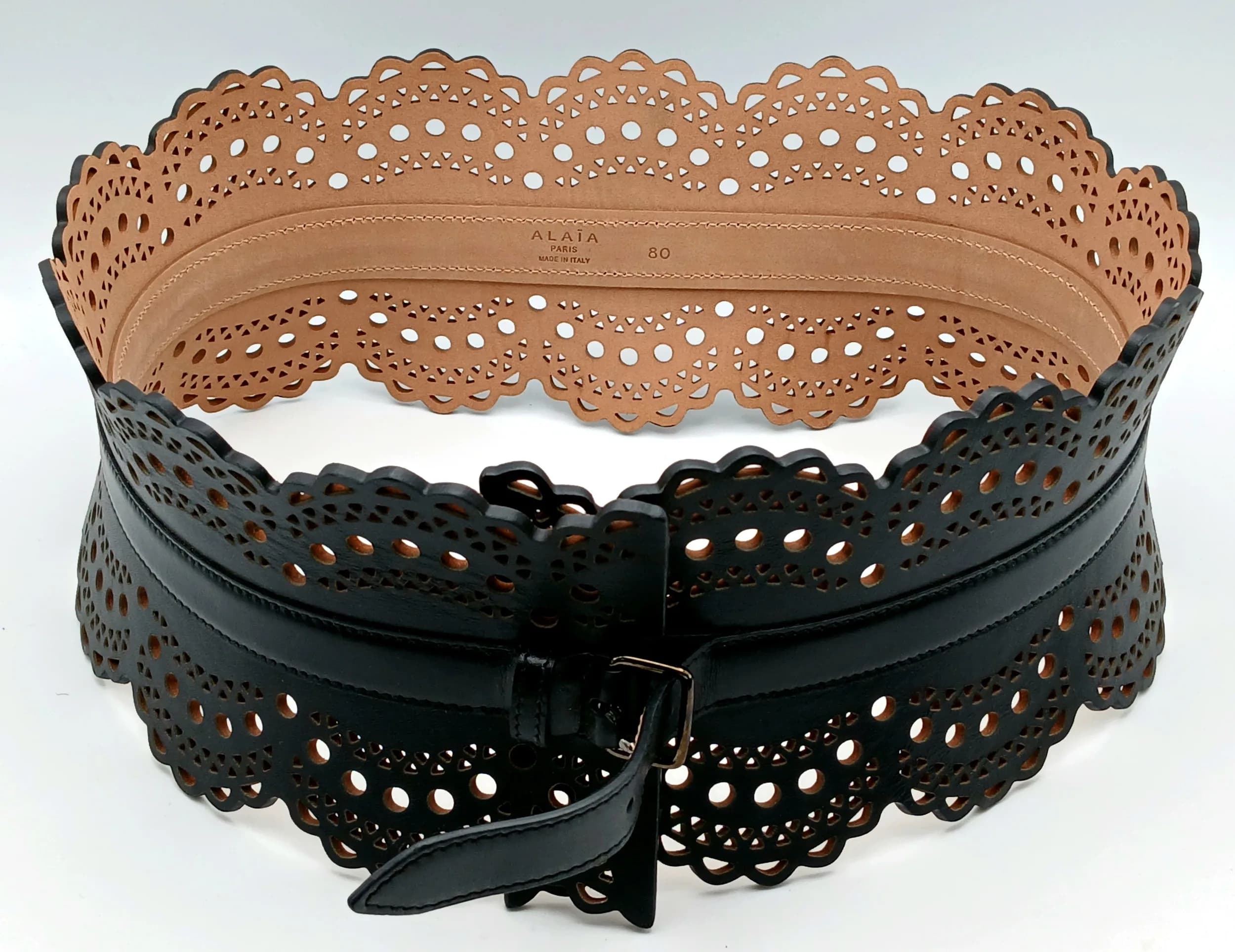 An Alaïa Wide Laser Cut Leather Waist Belt. Black leather with intricate laser cut geometric detailing, scalloped edges and a slim wraparound strap with buckle fastening. Approx. 82cm length x 11cm width. Comes with box. Some marks and signs of use to the leather. Please see photos or request a condition report. Ref: 29393.