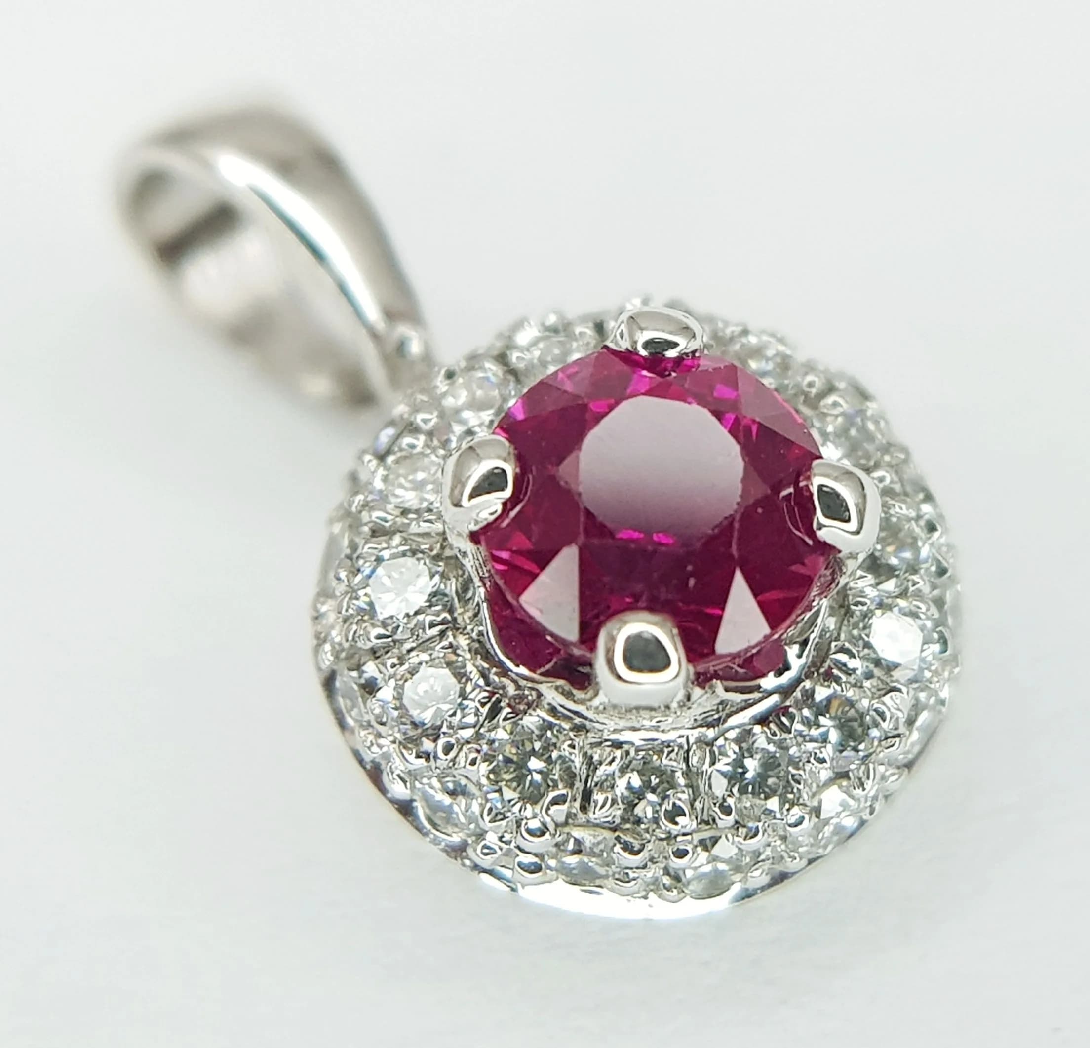 An 18K White Gold Ruby and Diamond Pendant. 14mm. A 0.30ct ruby with a 0.20ct diamond surround. 1g. MT32.