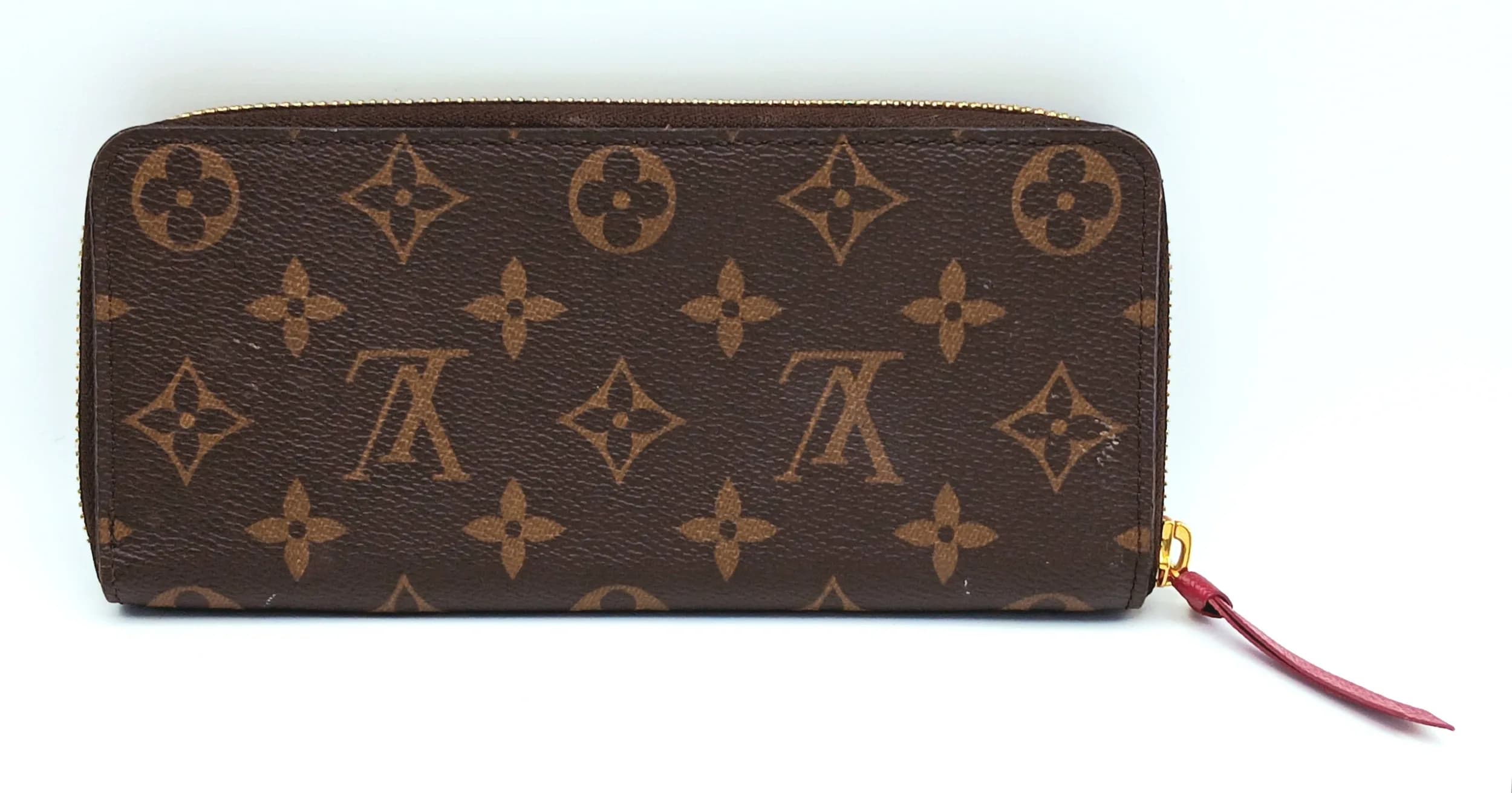 A Brown Louis Vuitton Monogram Zippy Wallet. Brown Monogram coated canvas exterior with gold-toned hardware, zip-around closure and burgundy leather zip pull. Fuchsia leather interior with multiple card slots, note compartments, two large compartments and a central zipped coin pocket. Approx. 19cm length x 9cm height. Some stains and marks to the leather but in fair condition overall. Please see photos or request a condition report. Ref: 29456.
