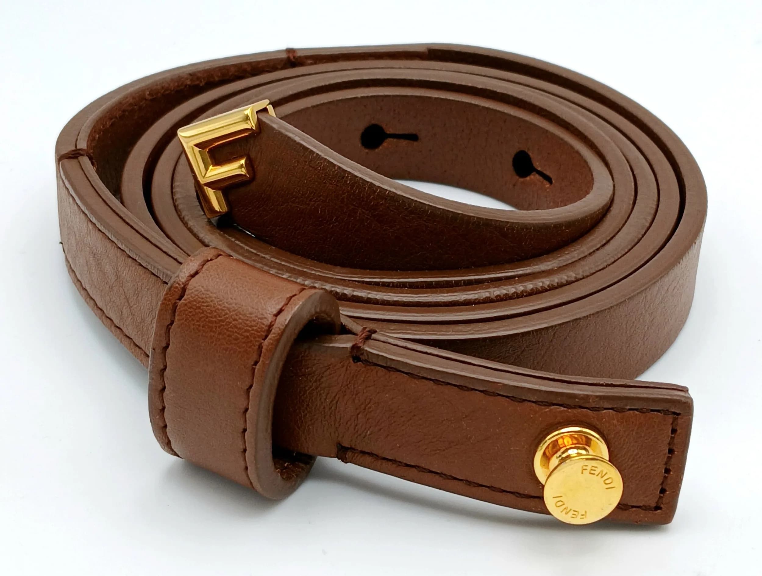 A Fendi Brown Leather Belt. Brown leather with gold-toned hardware and adjustable buckle fastening. Approx. 130cm total length. Some signs of wear to the leather and scratches to the hardware. Comes with a dust cover. Please see photos or request a condition report. Ref: 29425.