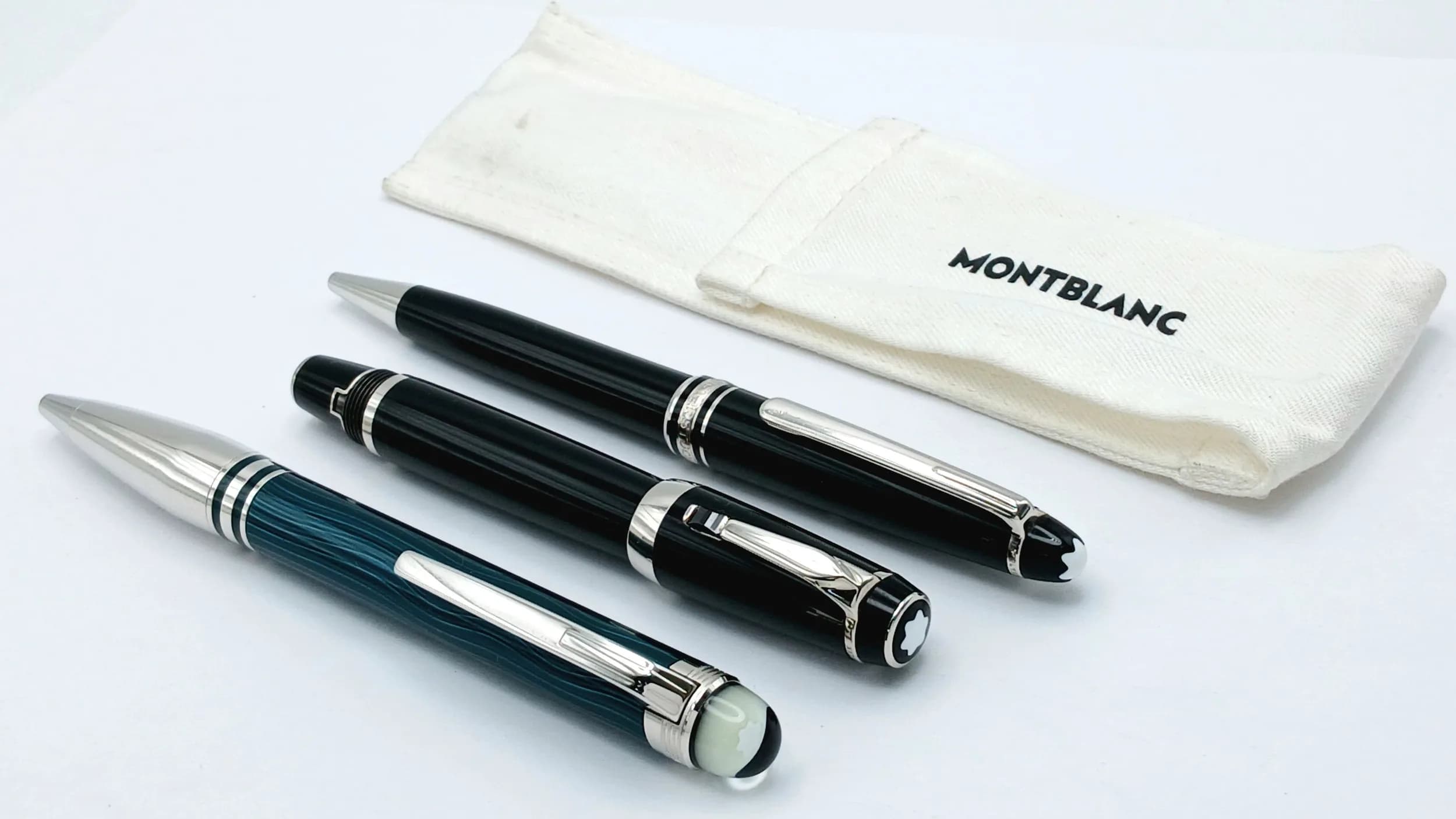 A Collection of Three Montblanc Pens. Comprising a green striped ballpoint pen, a black Meisterstück ballpoint pen, and a black Meisterstück fountain pen. Silver-tone trim throughout. The ballpoint pens each measure approx. 14cm length. The fountain pen measures approx. 11cm length. Please see photos or request a condition report. Ref: 29364.