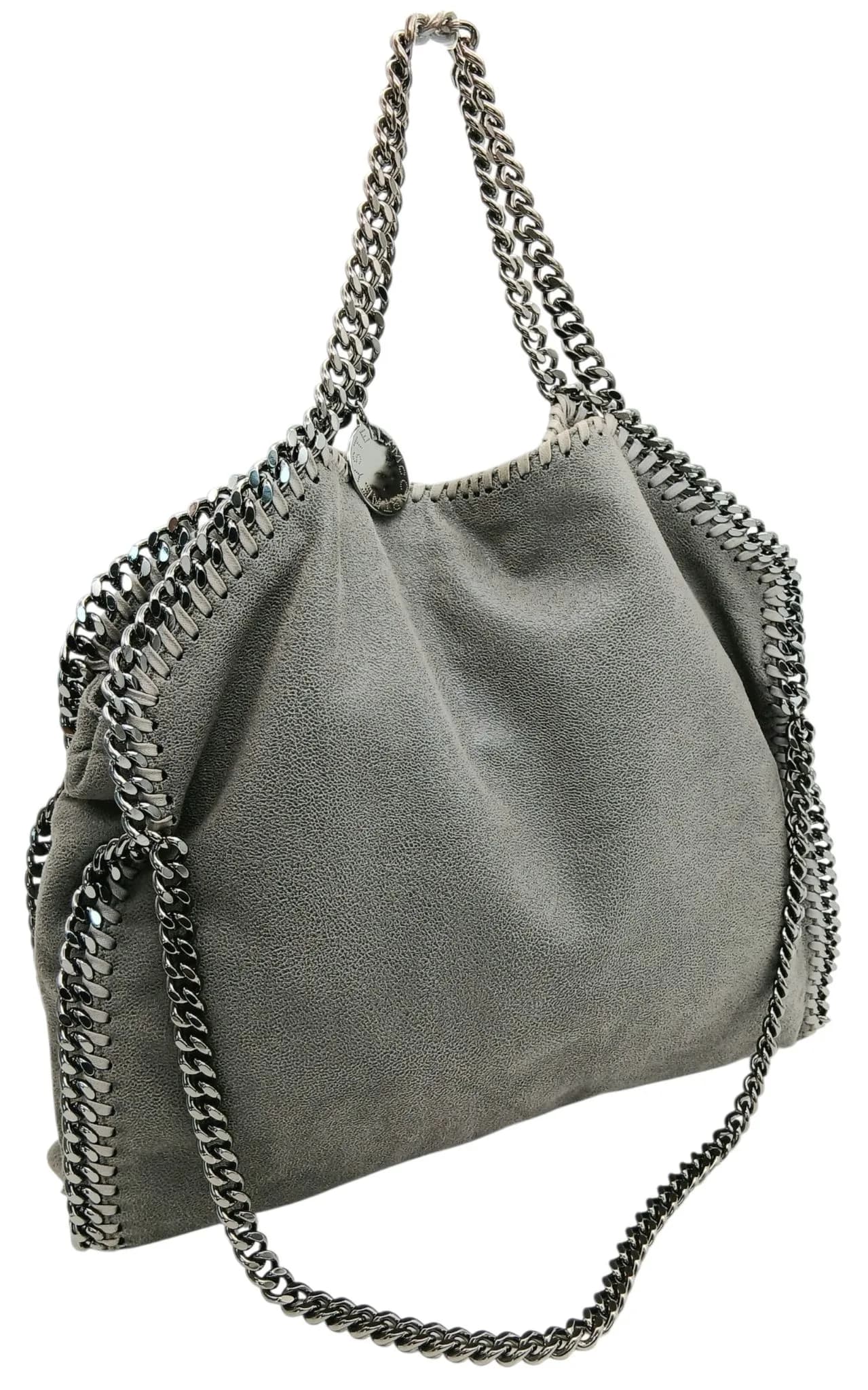 A Grey Stella McCartney Falabella Fold Over Tote Bag. Grey leather exterior with silver-tone hardware, chain trim, chain shoulder handles and magnetic closure. Pink textile interior with one main compartment and a zipped side pocket. Approx. 35cm length x 29cm height x 7cm depth. Comes with a dust cover. Some signs of wear, marks to the leather and scratches to the hardware. Please see photos or request a condition report. Ref: 29516.