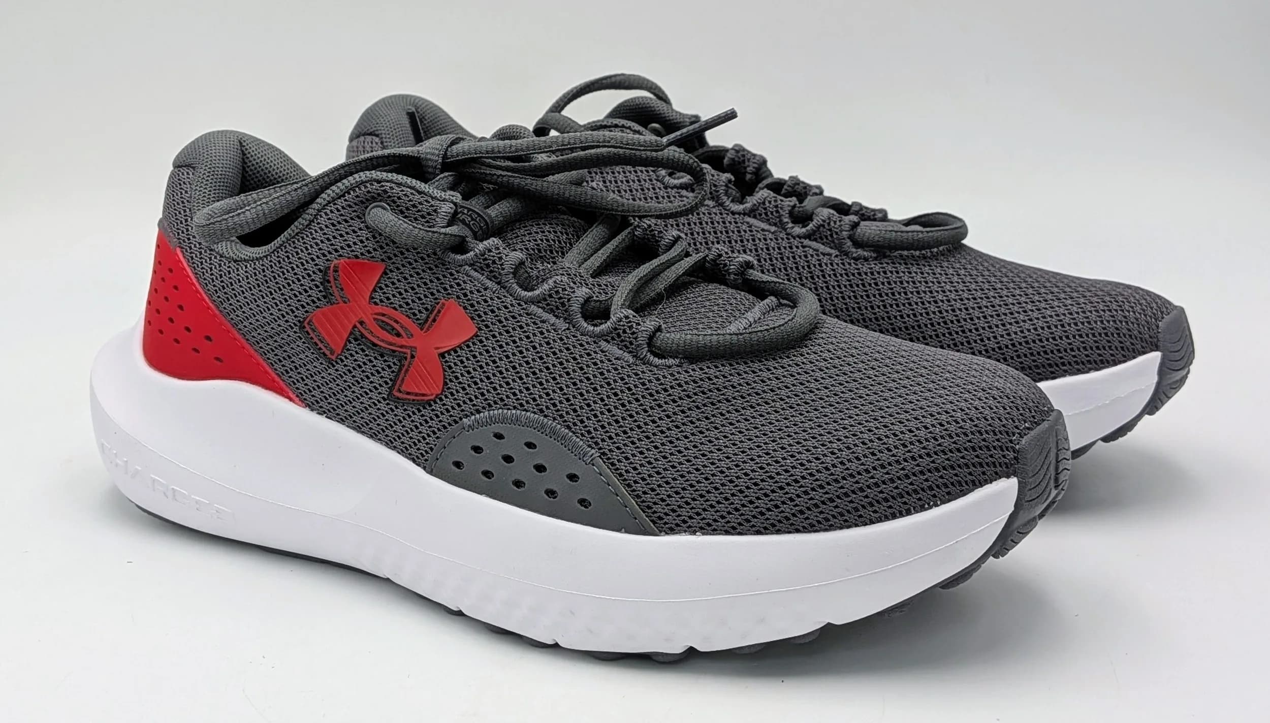 A pair of Under Amour charged surge 4 trainers, grey mesh with red accents. New without box. UK size 6, US size 7