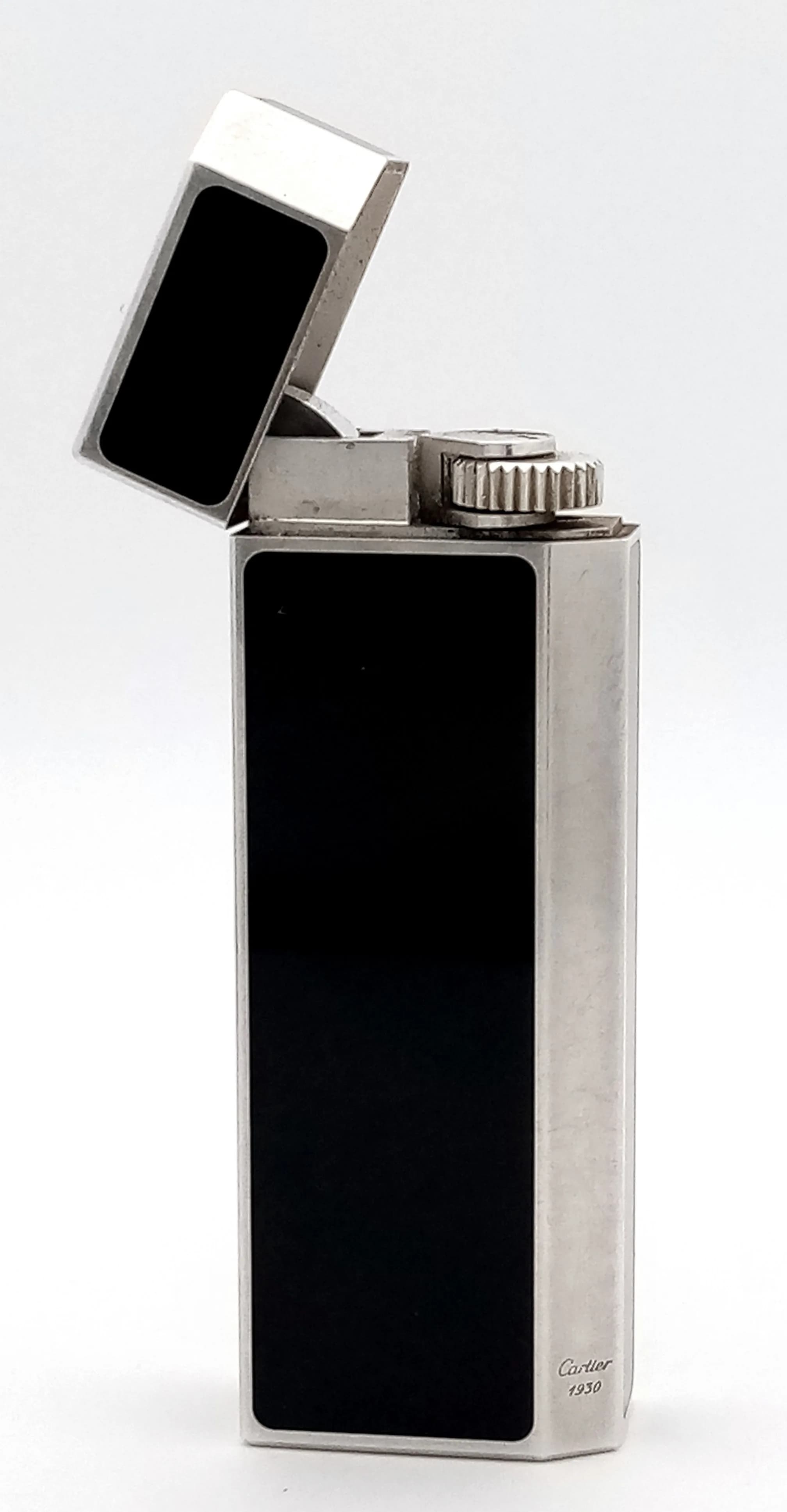 A Vintage Must de Cartier Lighter with Black Lacquer Panels.Cartier 1930 mark on silver tone side panel. Paris Cartier and serial number mark on base. Cartier Fitted case. 7cm. Comes with an additional Cartier red wallet. UK mainland shipping only.