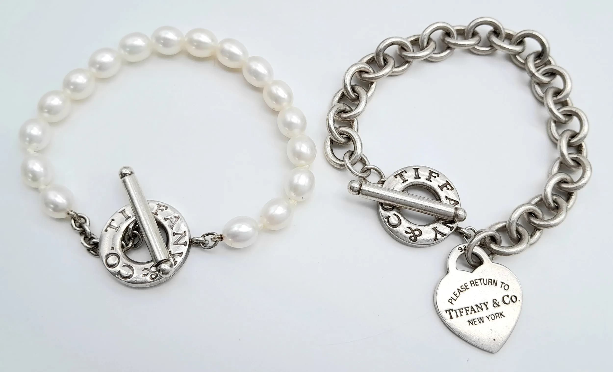 Two Tiffany and Co. Bracelets. Freshwater pearl with silver toggle clasp PLUS a classic circle link silver bracelet with toggle clasp and heart charm. 63g total weight. Ref: 029332.Both 18cm.