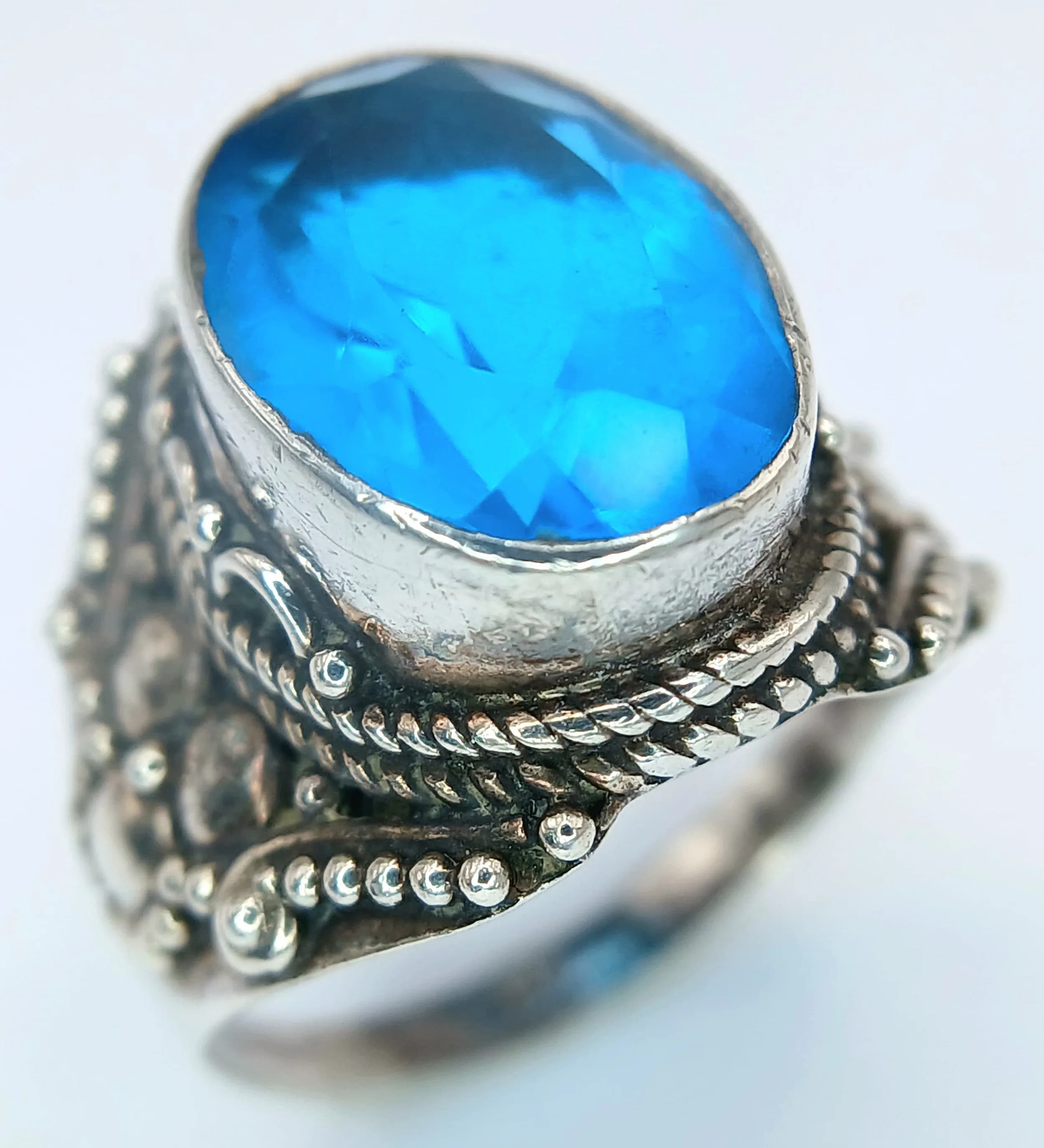 A Vintage Sterling Silver Blue Stone Ornate Detail Ring Size O1/2. The Ring measures 1.4cm Length at the Crown and has a gross weight of 6 grams.