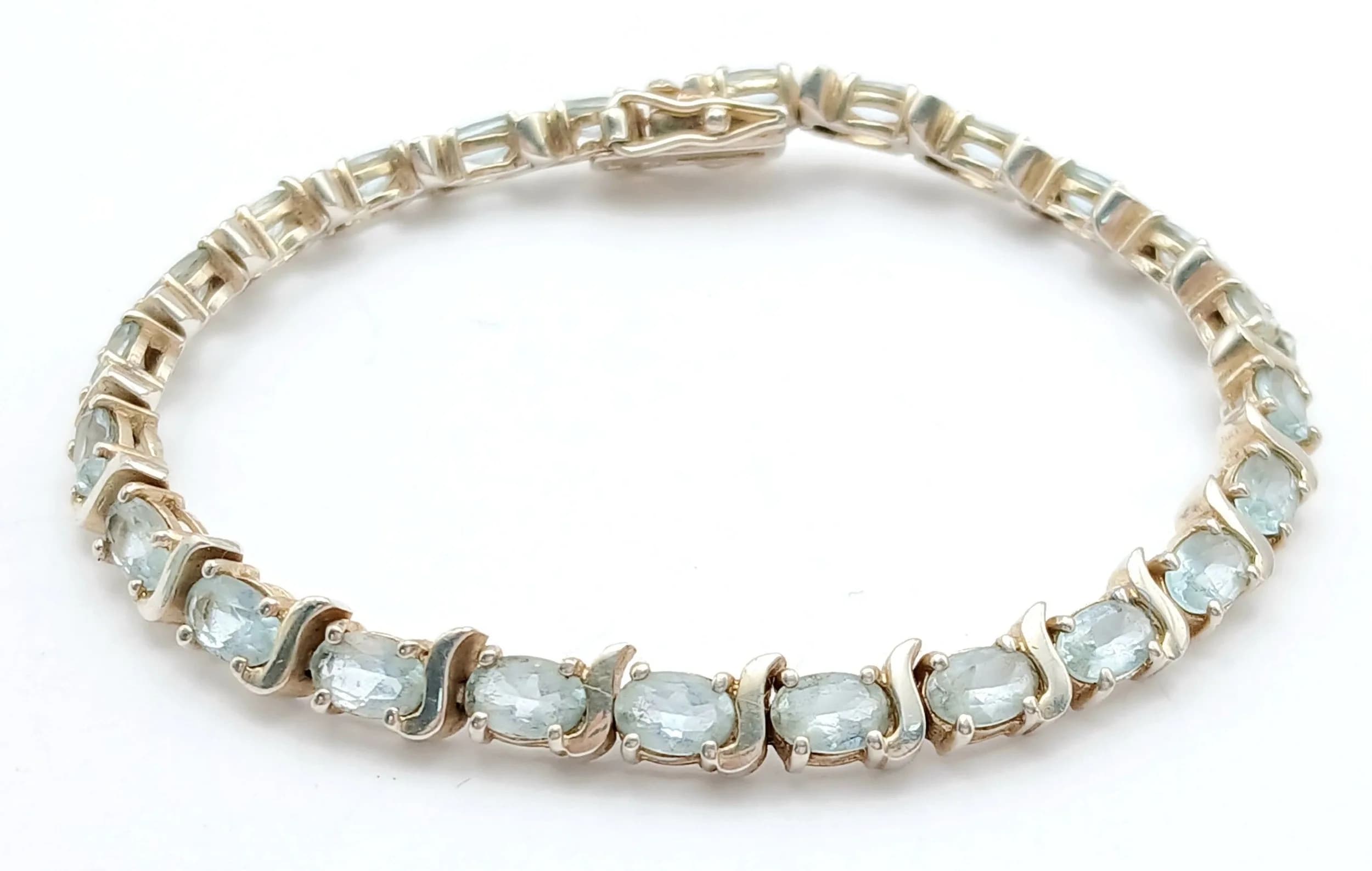 A Stylish Sterling Silver Blue Topaz Set Tennis Bracelet-19cm Length. Set with Twenty-Four 6 x 4mm Oval Cut Blue Topaz, circa 12 carat total. The Bracelet weighs 6.61 grams.