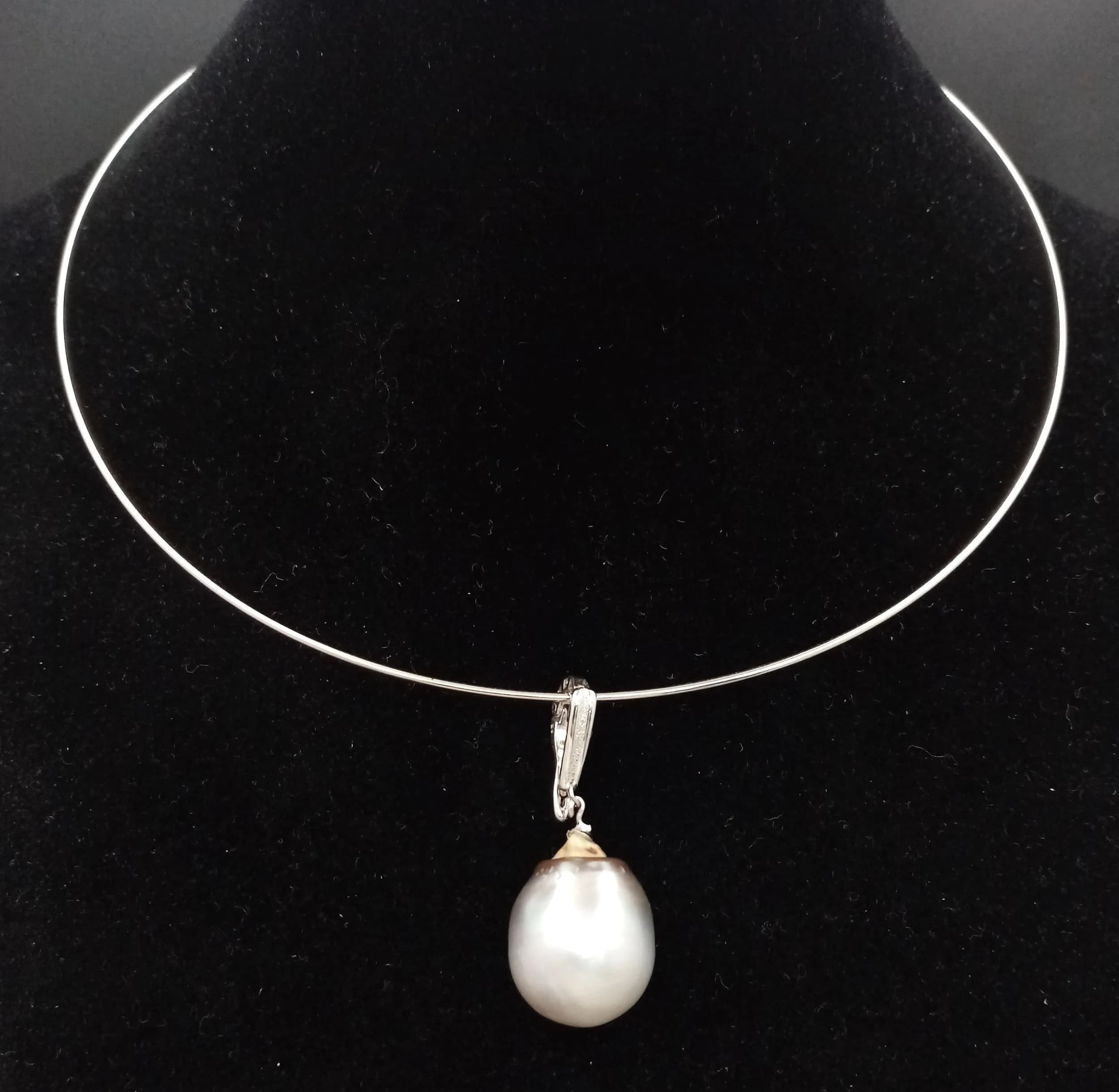 A Silver Pearl Drop Choker Necklace. Featuring a rigid silver tone wire necklace with a large baroque freshwater pearl drop pendant and decorative bail.