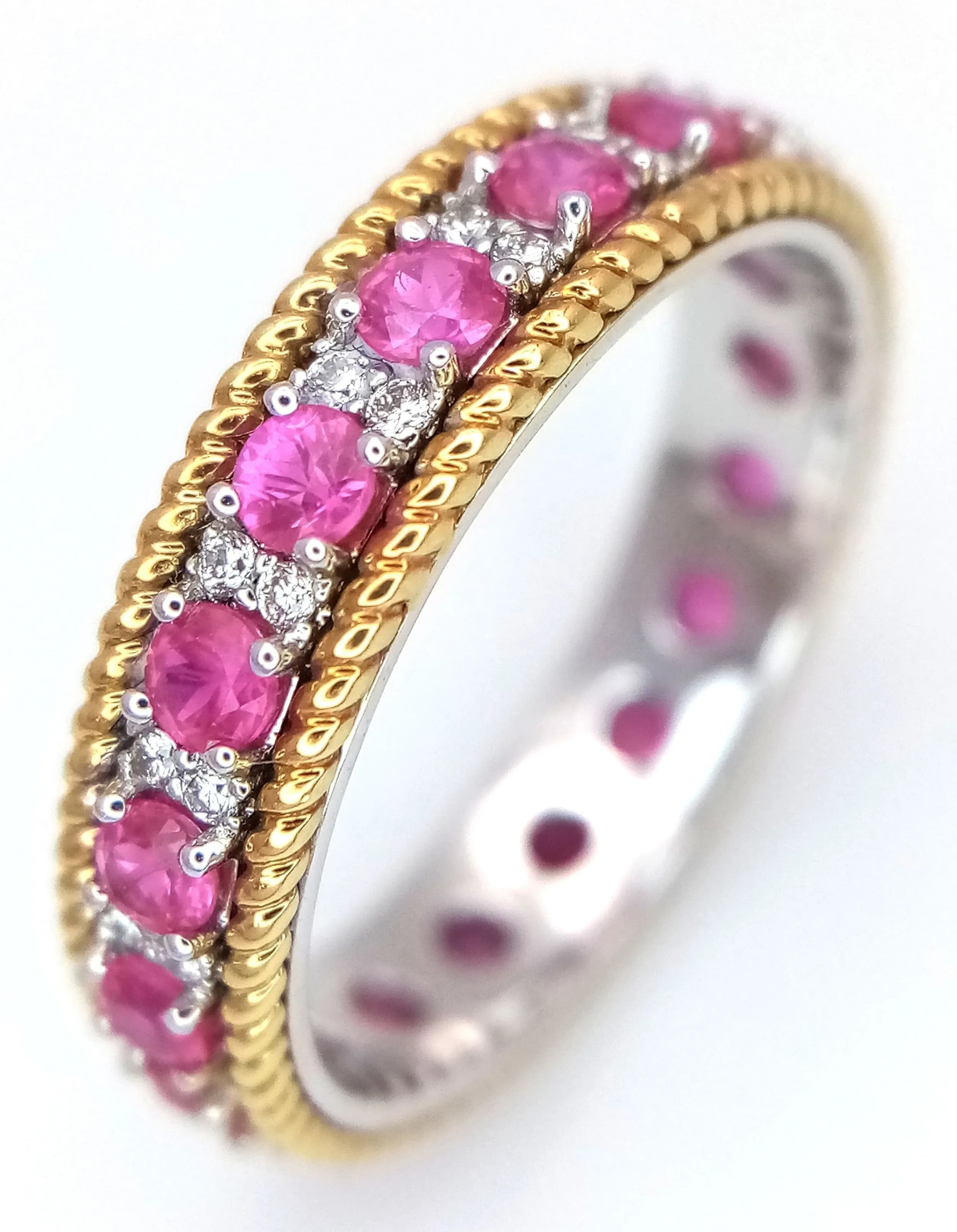 AN 18K WHITE GOLD, WITH YELLOW GOLD BEADED EDGE, DIAMOND AND RUBY SET, FULL SET BAND RING. 1.21CTW OF RUBIES AND 0.19CTW OF DIAMONDS. 4.3G, SIZE M. SSPA 5006