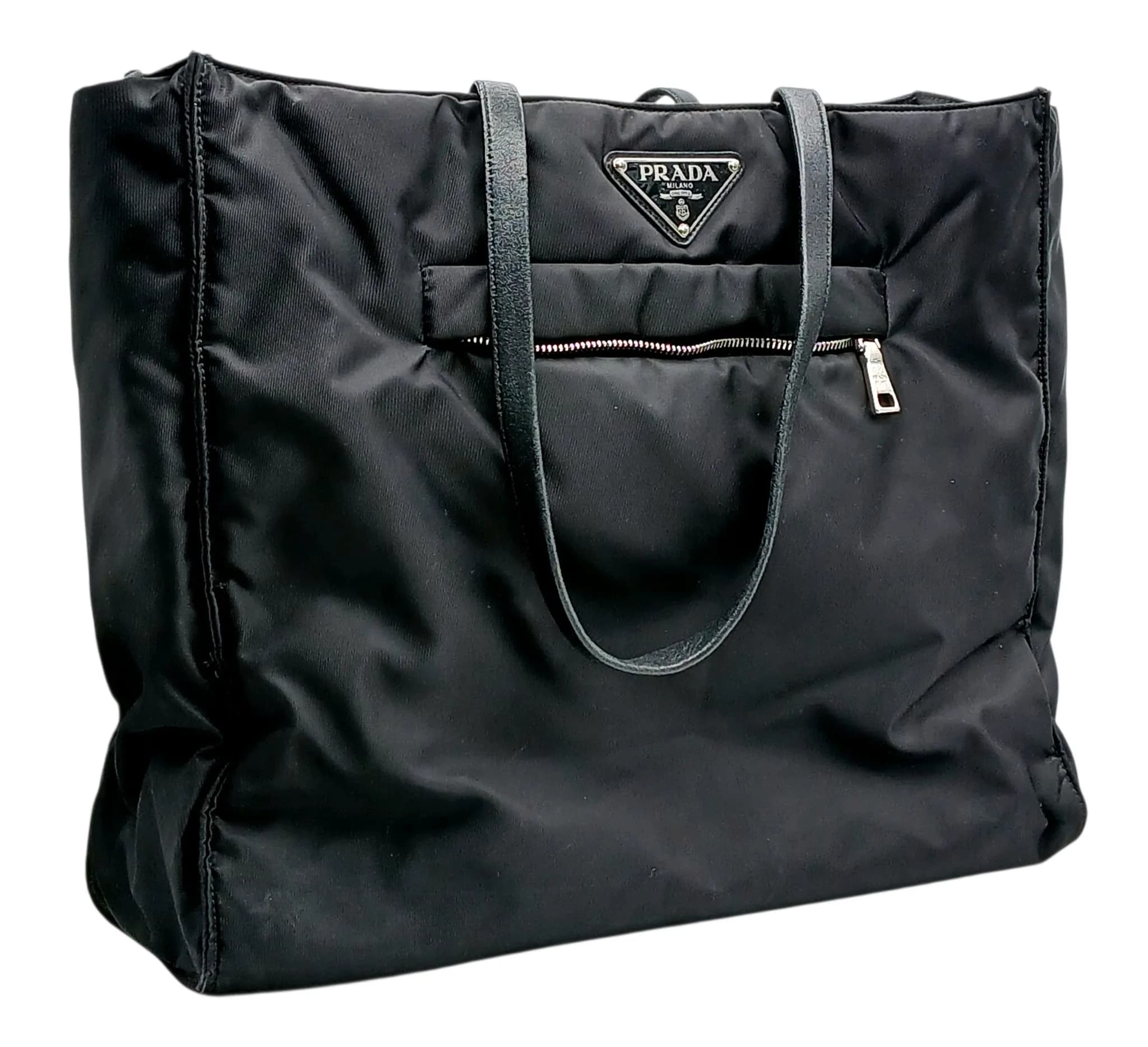 A Black Prada Tessuto Nylon Tote Bag. Black nylon exterior with black leather twin shoulder handles, silver-toned hardware, front zip pocket and open top. Black textile interior with one main compartment and two zipped pockets. Approx. 36cm length x 31cm height x 12cm depth. Some signs of wear and marks to the textile. Comes with a certificate of authenticity. Please see photos or request a condition report. Ref: 29347.