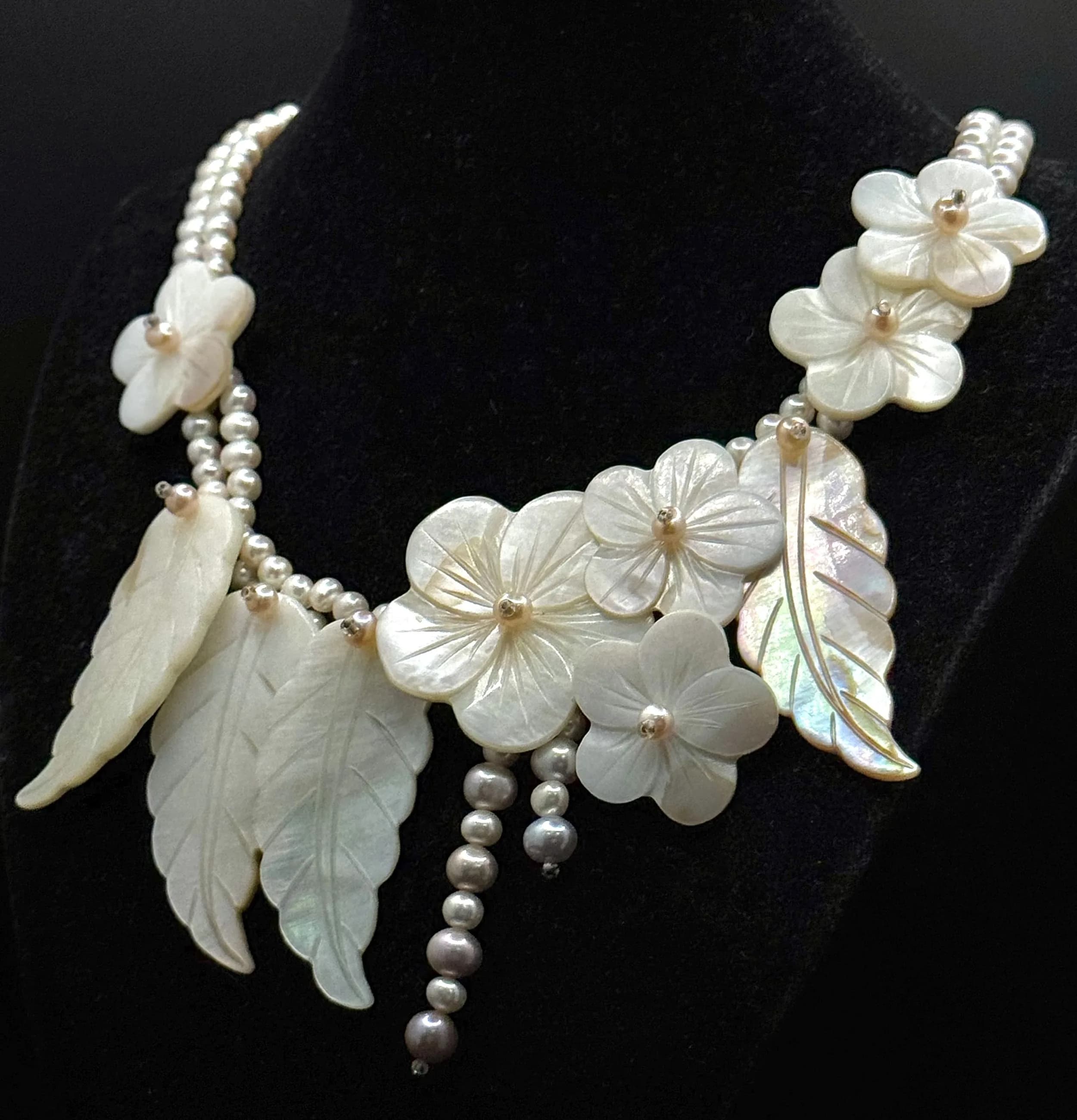 A Beautiful Freshwater Pearl and Mother of Pearl Floral Statement Necklace. Triple strand freshwater pearl necklace with a large carved mother of pearl floral and leaf centrepiece. Fitted with a 925 silver clasp. Approx 46cm length with a 6cm pendant drop.